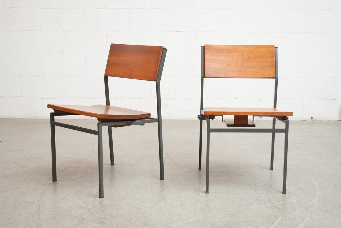 Beautifully constructed teak stacking chairs with gray enameled metal frame and book cubby under seat. Hooking mechanism on the sides to make rows. In original condition with some visible wear to wood and frame consistent with age and use. One cubby