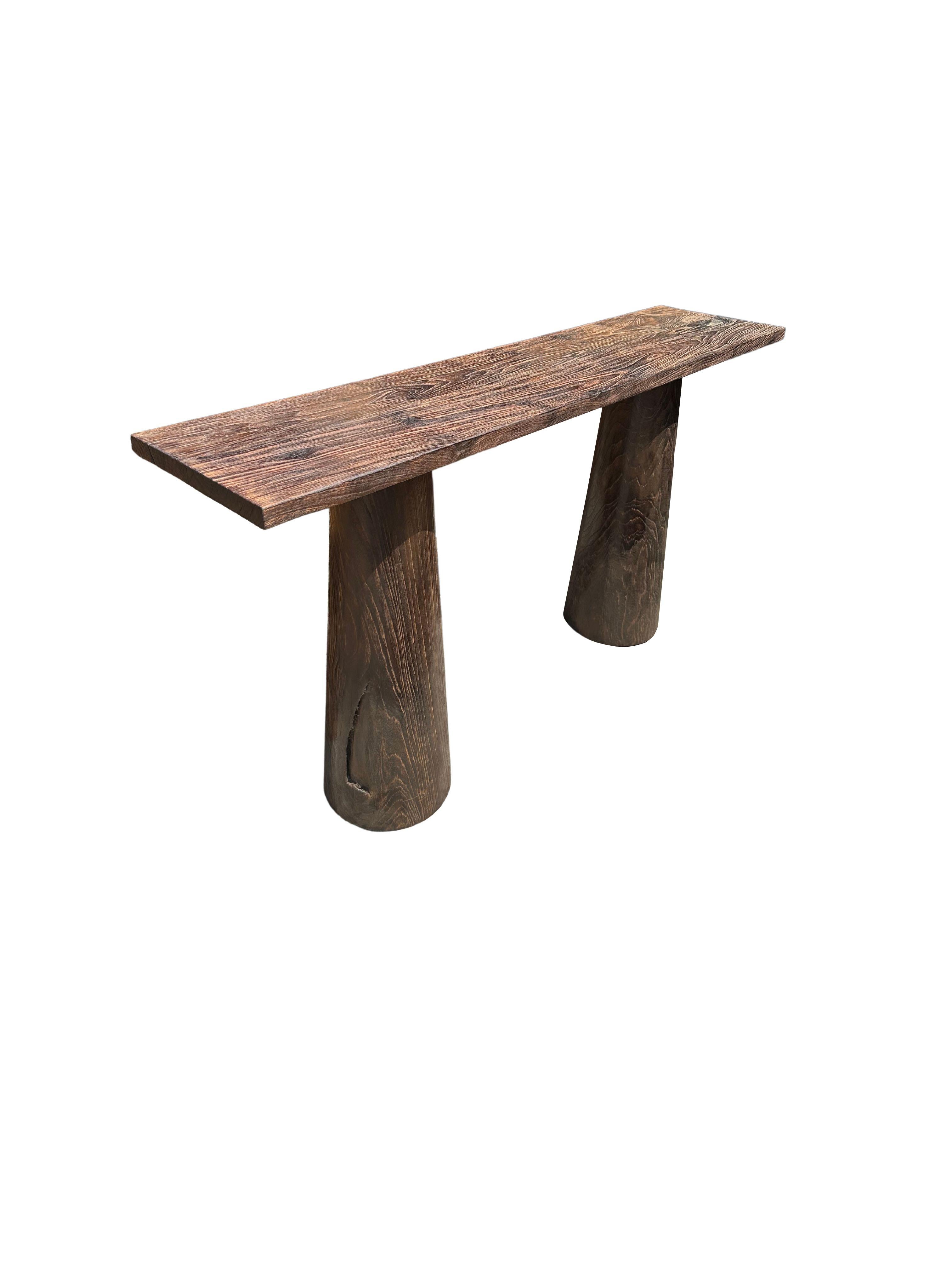 A sculptural teak wood console table crafted from solid teak wood. The table top sits atop two solid,  legs. A wonderfully minimalist object. The subtle wood textures present on all sides adds to its charm. To achieve its unique pigment the wood was