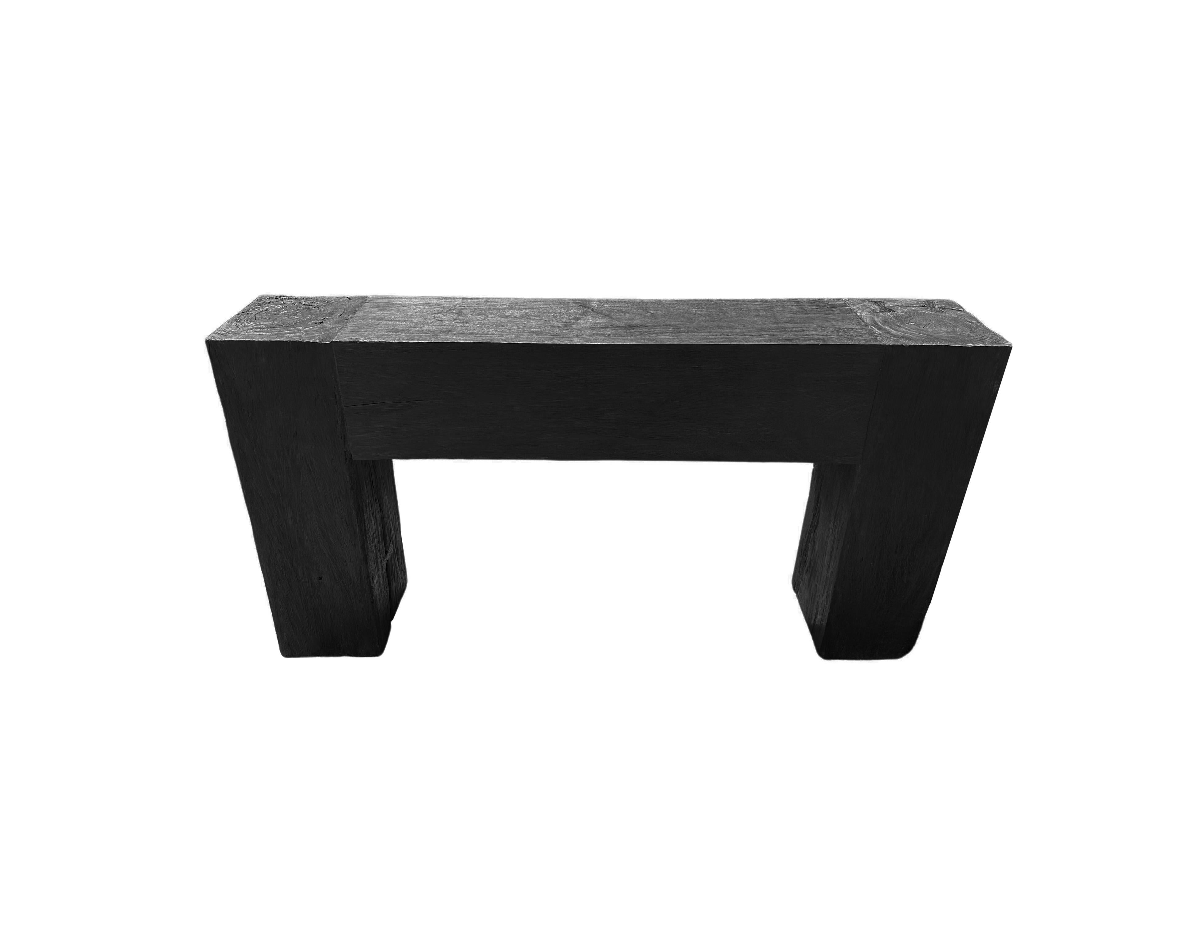 A sculptural teak wood console table crafted from solid teak wood. The table top sits atop two solid,  legs. A wonderfully minimalist object. To achieve its unique pigment the wood was burnt several times and then finished with a clear coat. The