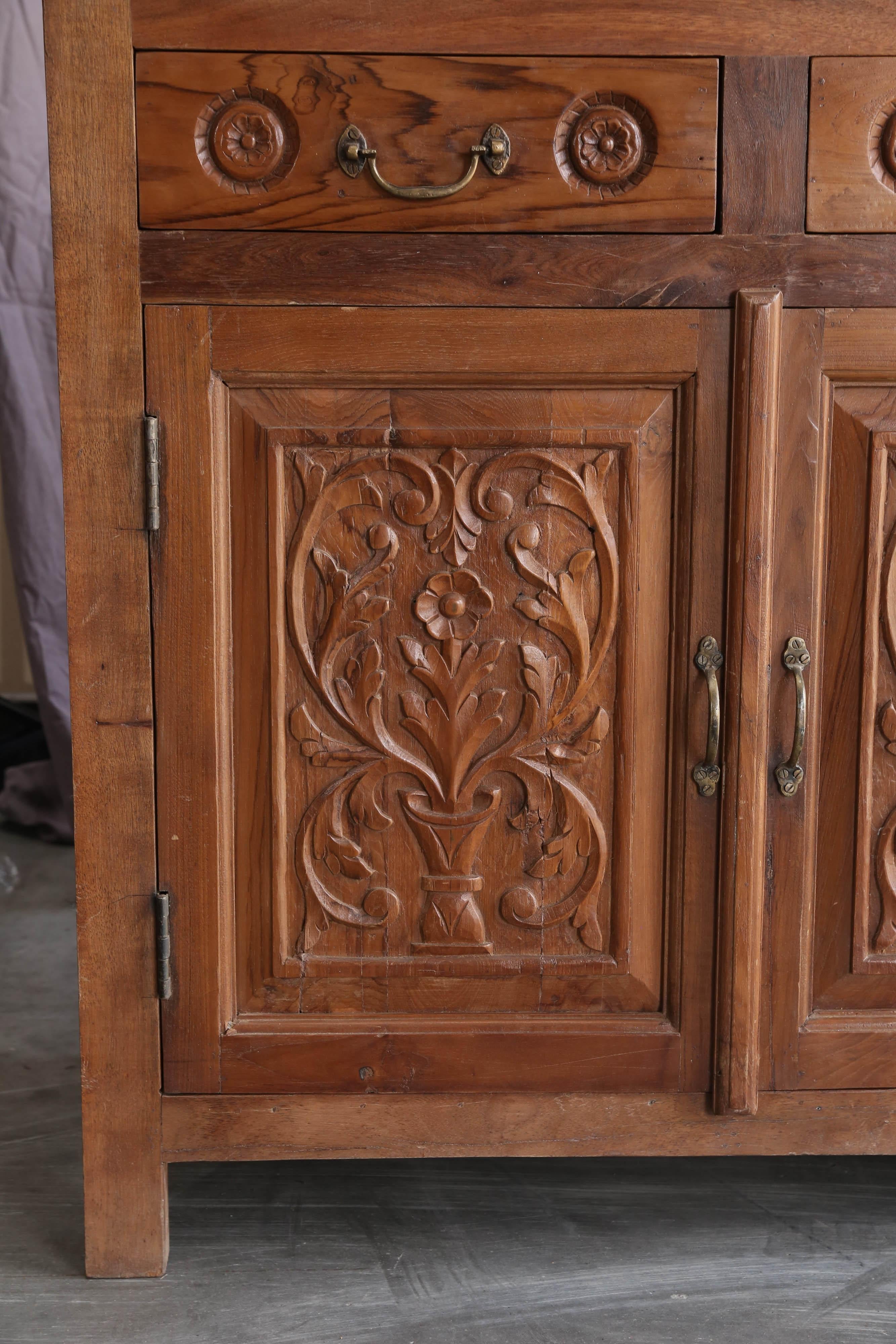 Fine quality Burmese teak wood is used in making this four-door simple yet elegant credenza. It has four upper drawers and supported on four plain legs. It retains original hand made brass hardware. The carving on this piece is crisp and smooth.