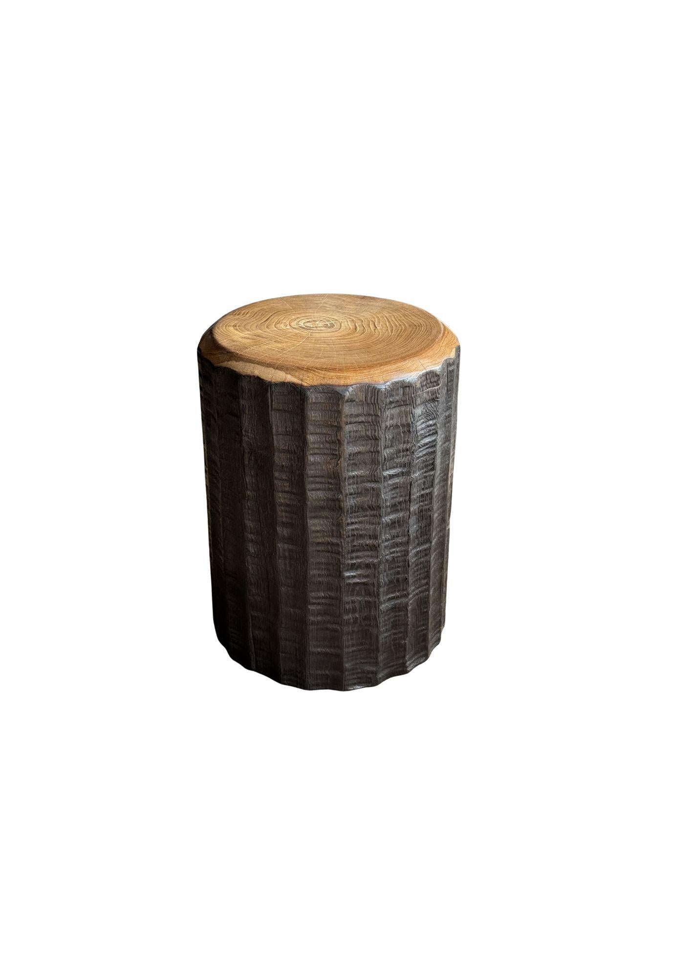 A wonderfully sculptural round side table. Its neutral pigments make it perfect for any space. It was crafted from a solid block of teak wood and features carved detailing on its sides. The wood textures and shades present on all sides adds to its