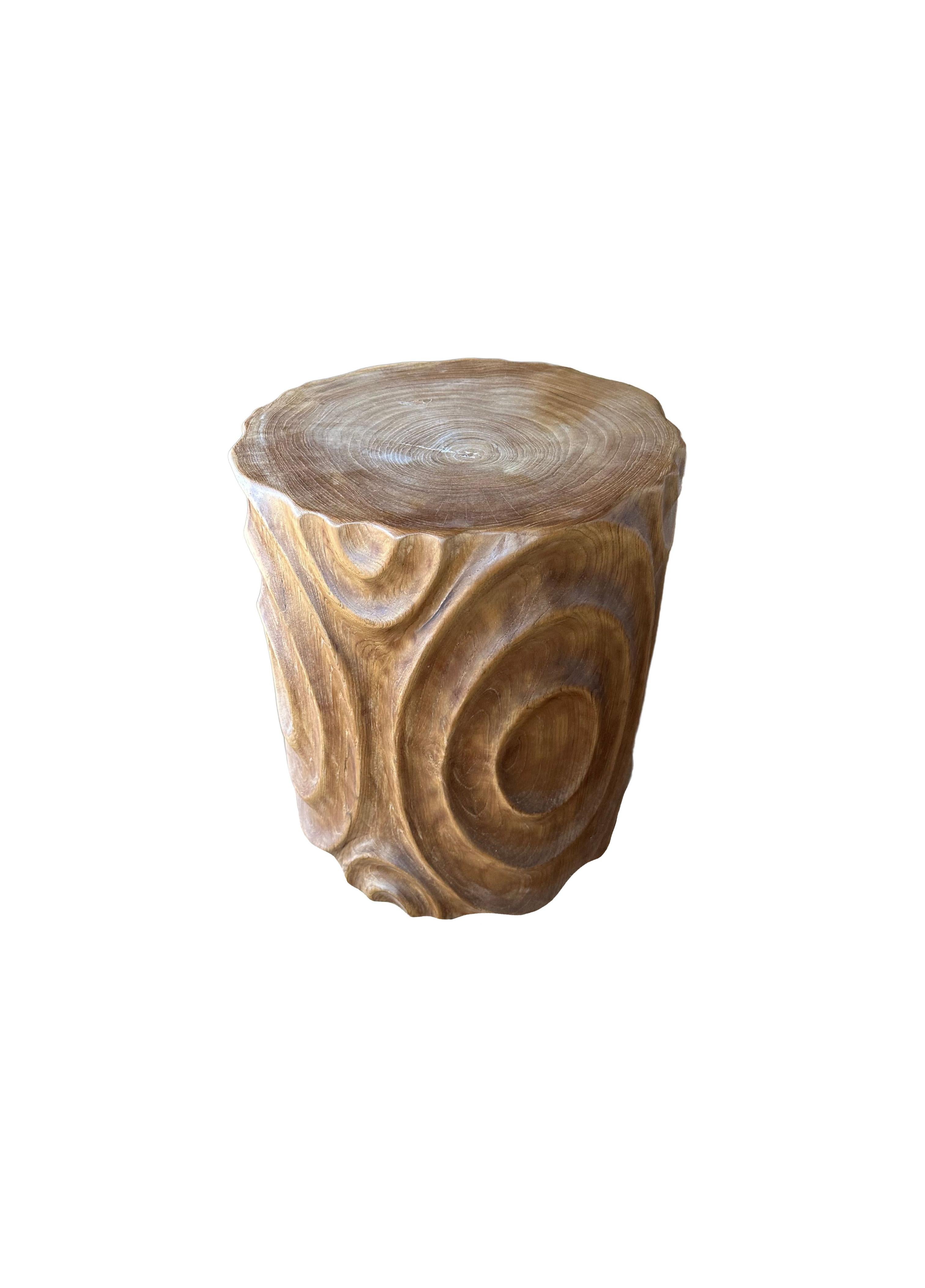 A wonderfully sculptural round side table. Its neutral pigments make it perfect for any space. It was crafted from a solid block of teak wood and features carved detailing on its sides. The wood textures and shades present on all sides adds to its