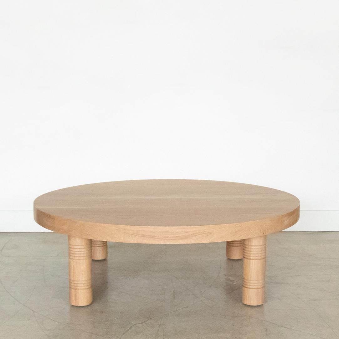 Solid white oak circular coffee table with four post legs and carved ribbed detailing; inspired by French design. Made in Los Angeles.