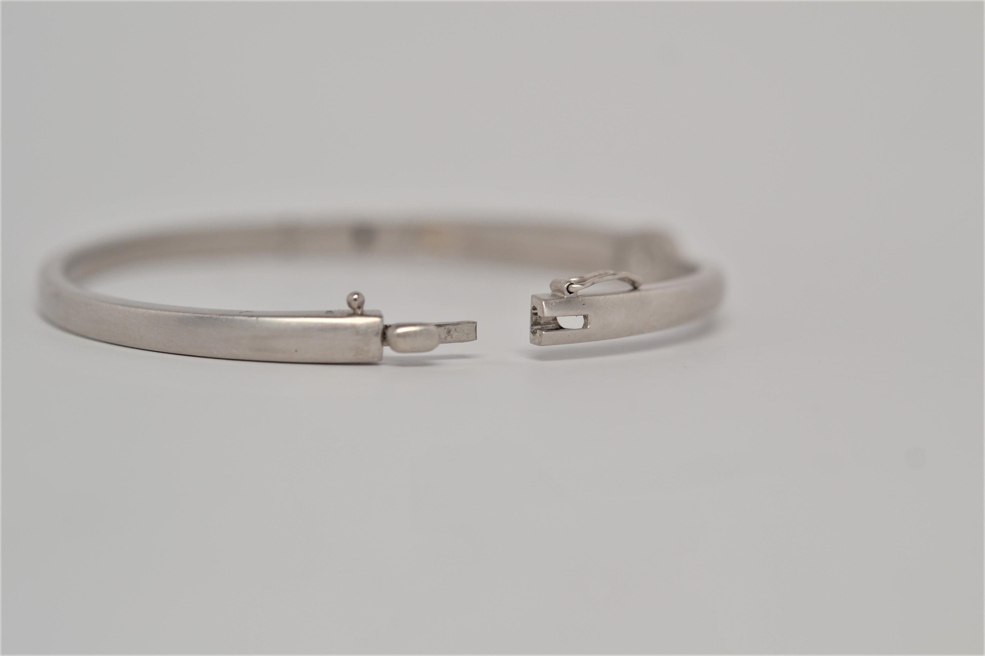 A simple 14k White Gold bangle bracelet set with one Round Brilliant Cut Diamond. The solitaire bangle layout is hinged with a push clasp and secondary lock, polished with a brushed finish. A Round Brilliant Cut Diamond weighing 0.48ct is set inside