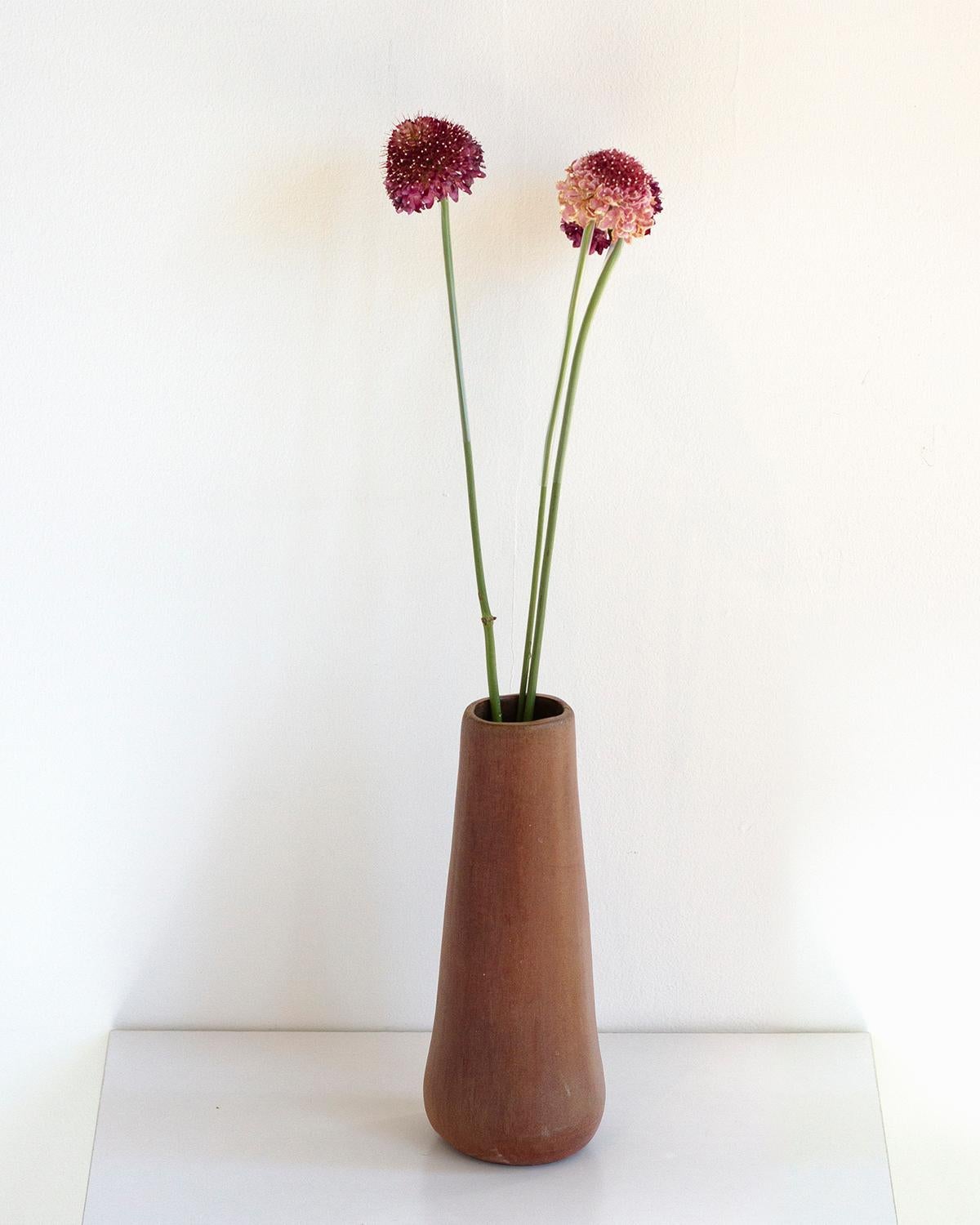 This Solitaire Clay Vase is crafted from toasted clay and is perfect for displaying flowers, branches, or other decorations in minimalist luxury. Its rustic brown hue adds to its quiet elegance, and it makes for an ideal holiday gift. Each piece is