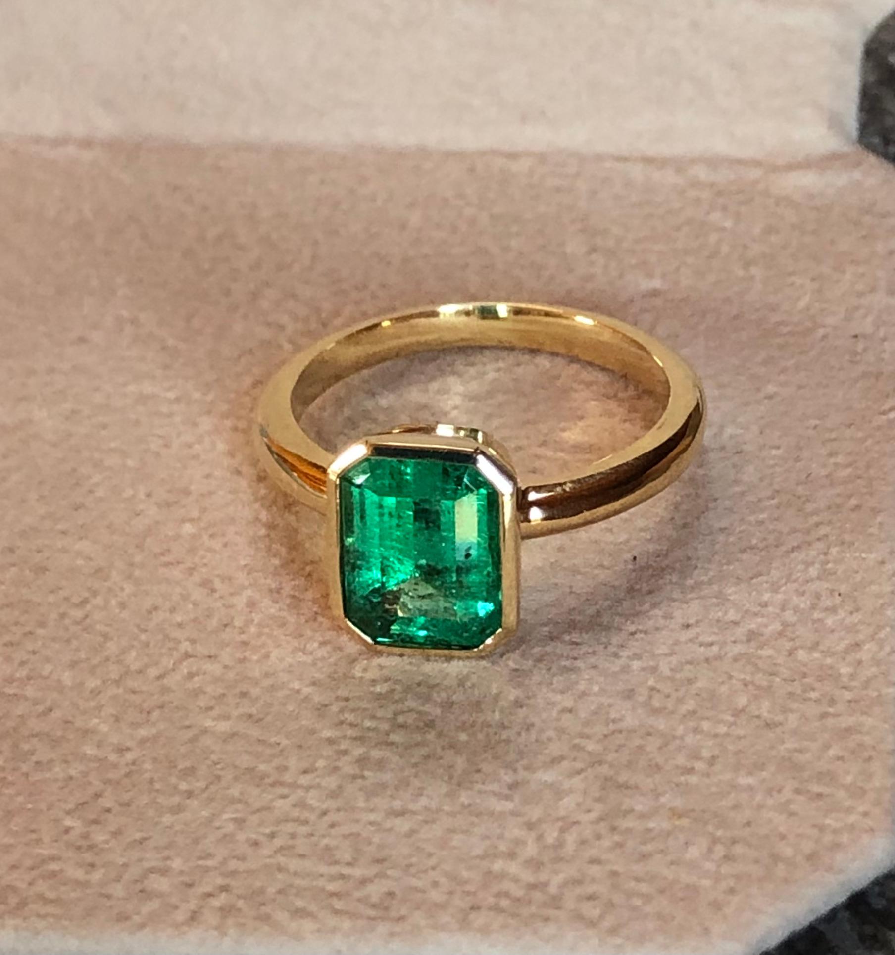 This is a stunning emerald bezel set solitaire engagement ring, the center stone is a natural Colombian emerald emerald cut weighing 2.32 carats. Lively medium green, VS clarity.  The engagement solitaire ring is made of solid yellow gold 18K. The