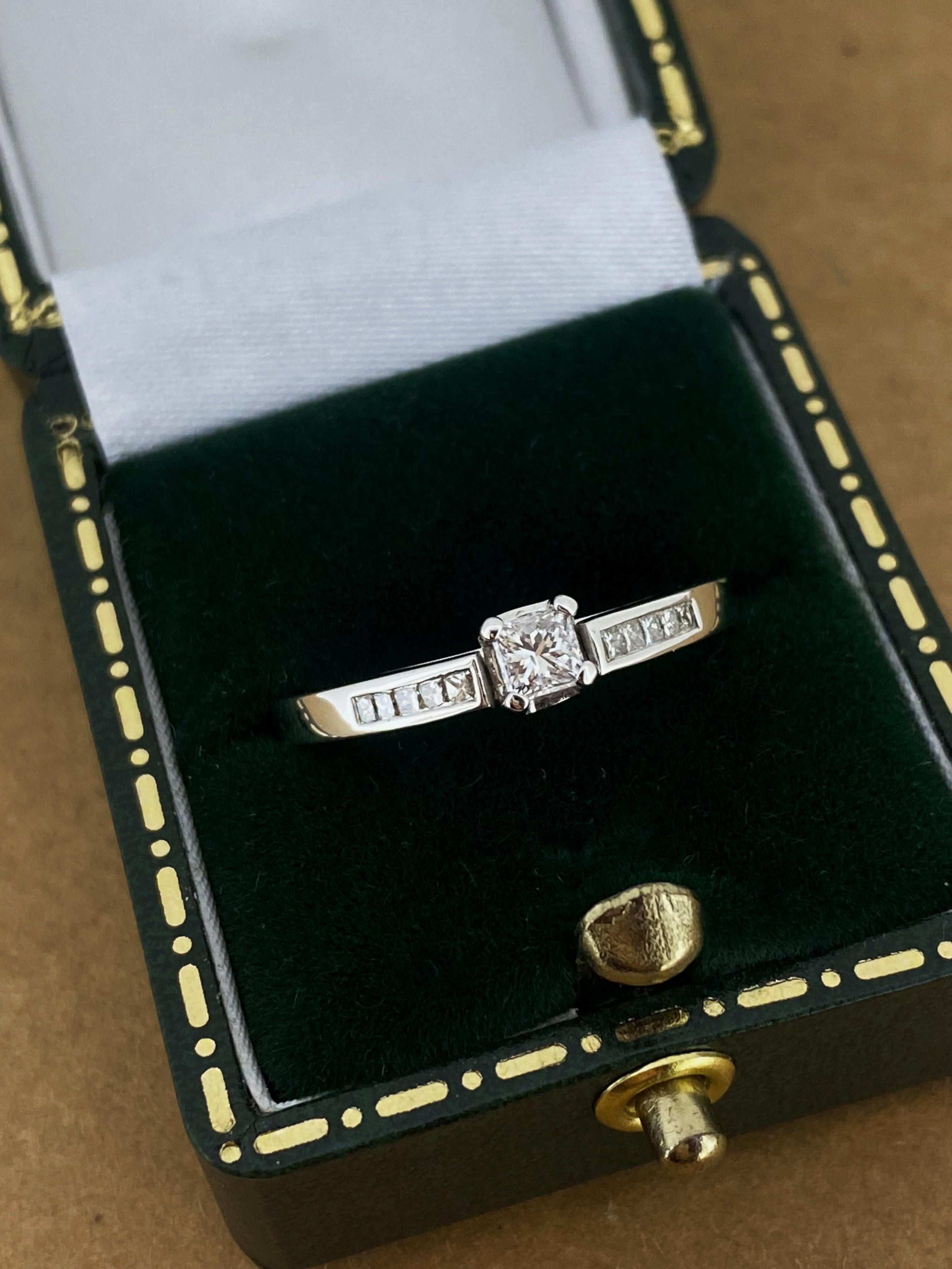 Of timeless & visually striking 
Solitaire with Accents design 
this piece is centrally 4-claw set with 
a sparkling Princess Cut Diamond, 
measuring 3.5mm approx. – 0.15ct approx.
of G colour, VS clarity & sun-like brilliance, 

Securely basket-set