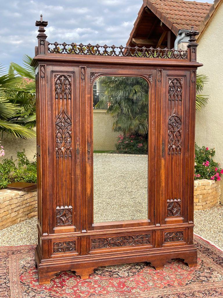 Superb neo-Gothic-style oak bedroom with a wardrobe, a bed and two bedside tables. The bed features a canopy and is richly carved with towel folds, ribs and arrowheads. The wardrobe has three doors and three drawers. The central door has a mirror