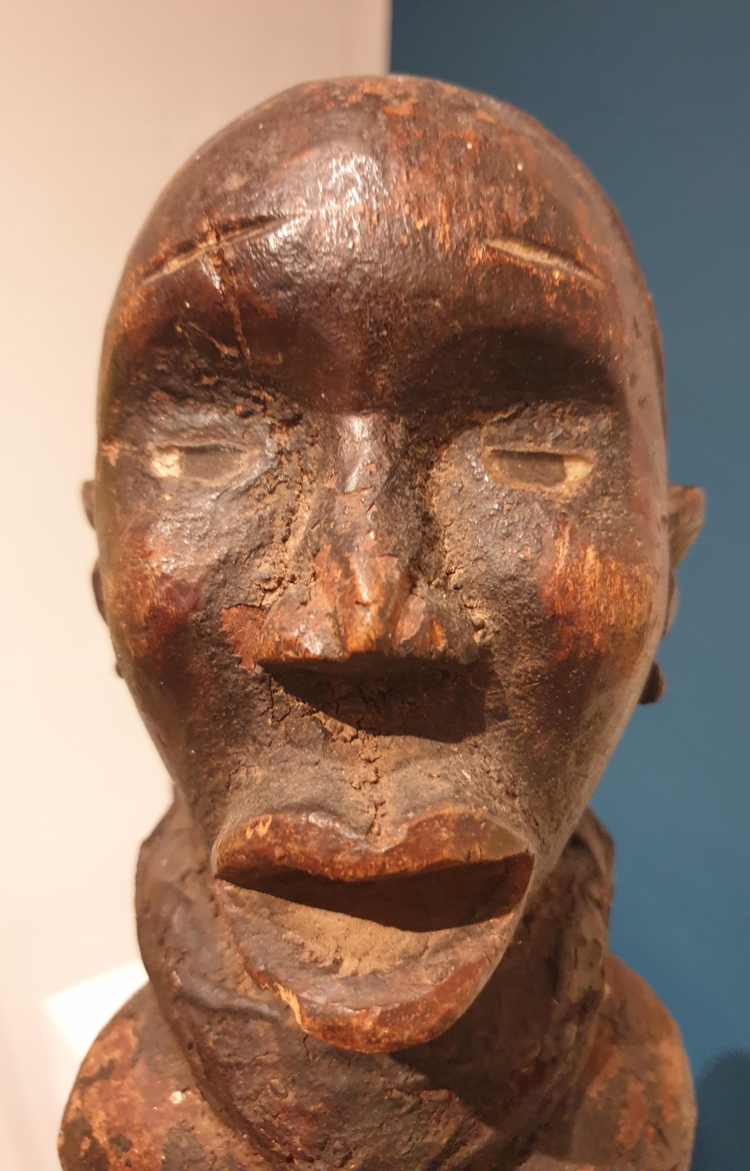 Männliche Songye-Power-Figur, Demokratische Republik Kongo, auf einem Knie ruhende männliche Figur mit durchbrochenen Armen und Händen, die auf dem Bauch ruhen, der verschiedene Charme und handgeschmiedete Gegenstände enthält; auf dem Rücken trägt
