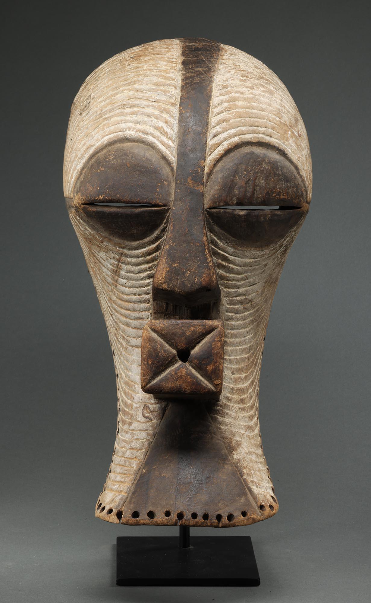 Aus Holz geschnitzte große weibliche Songye Kifwebe-Maske mit klassischen weißen Linien, geschwärztem Kamm entlang der Stirn, Nase und Mund.  Abgenutzte Löcher am hinteren Rand der Maske von der Befestigung des Kostüms.
Demokratische Republik Kongo,
