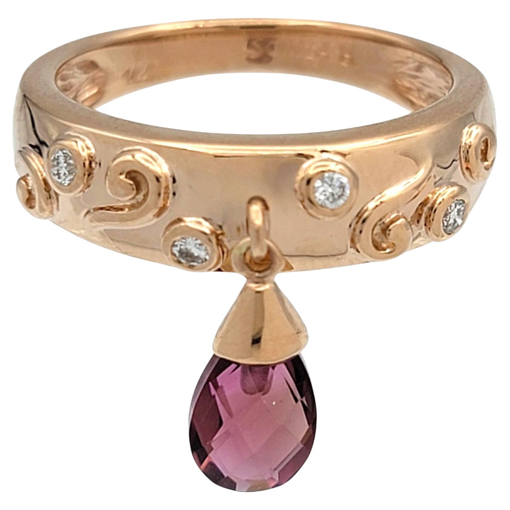 This Sonia B ring is a striking blend of bold color and refined elegance. At its heart rests a pear-shaped rhodolite garnet, cut in a mixed checkered style that captures light with vivid brilliance. The garnet’s deep dark pink hue radiates a rich