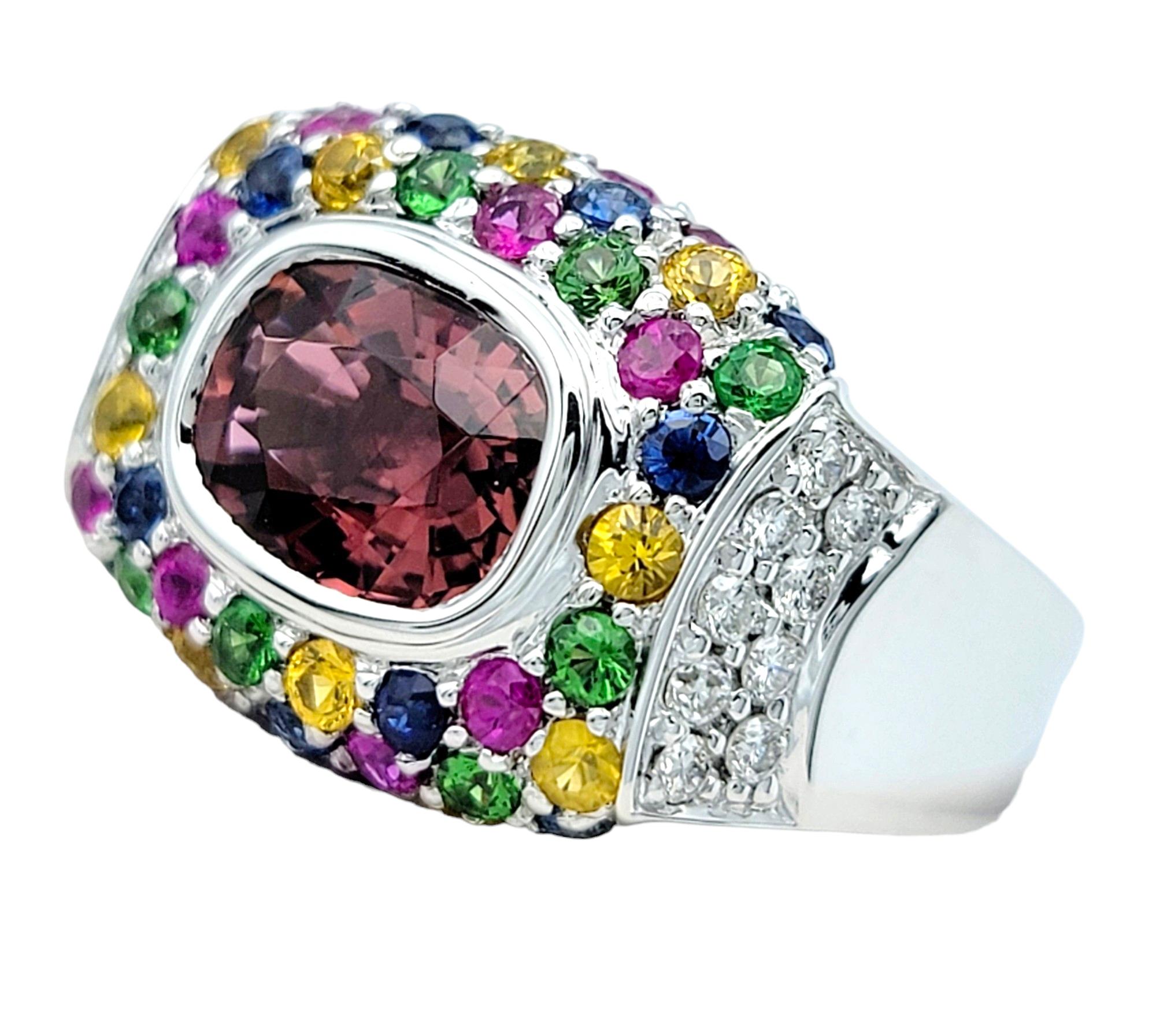 Ring Size: 7

This beautiful Sonia B. ring features a striking large cushion pink tourmaline as its centerpiece, encircled by an array of multicolored lab-grown sapphires, as well as natural round diamonds along the sides. Set in elegant 18 karat