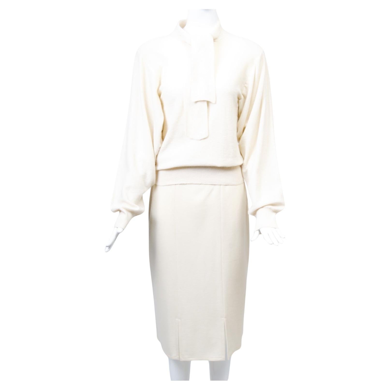 Quintessential Sonia Rykiel ensemble consisting of a pullover sweater and slim skirt in ivory wool knit, c.1980s. On top, the sweater is distnguished by a button opening in front and an attached tie in ribbed knit, while the body is crafted of fine