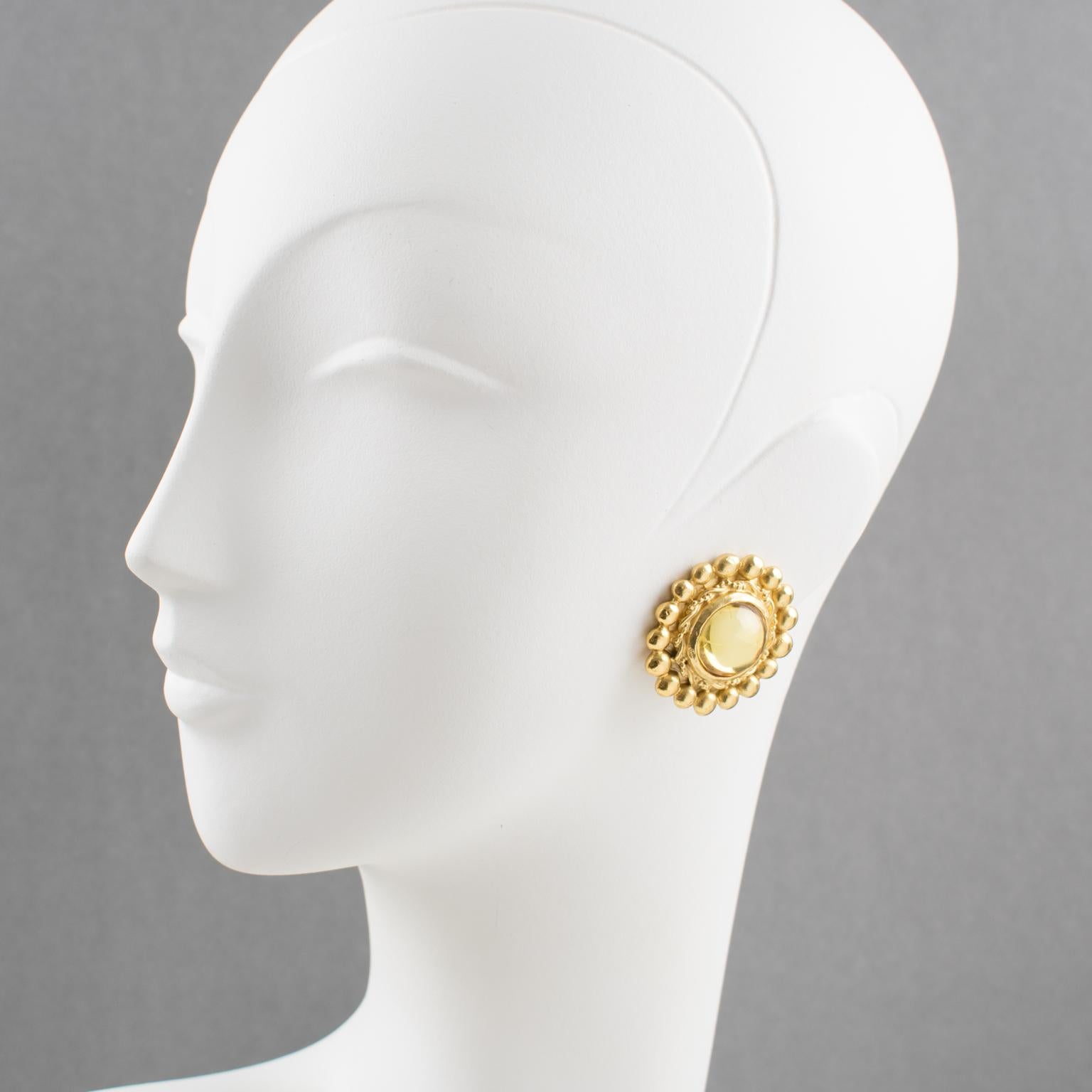 Elégantes boucles d'oreilles à clip signées Sonia Rykiel Paris, créatrice de mode française. Elles présentent une forme arrondie en métal doré avec texture, surmontée d'un grand cabochon en résine de couleur jaune clair champagne. Signé en dessous :