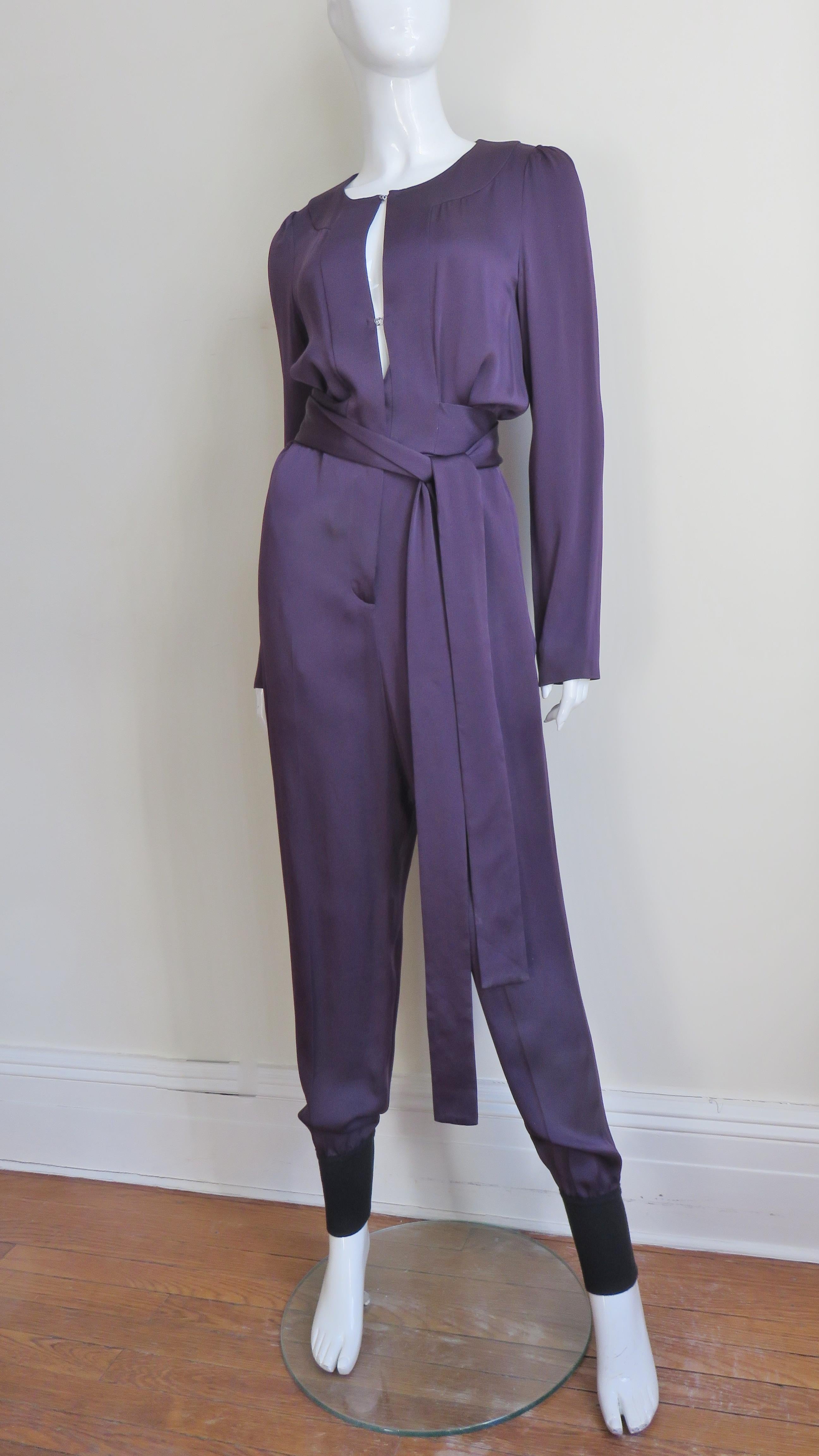 A fabulous eggplant purple silk jumpsuit from Sonia Rykiel. The jumpsuit has long sleeves, cuffed full pant legs, hip side seam pockets and a long belt wrapping around the waist.  It has a keyhole front closing with several silver hooks revealing a