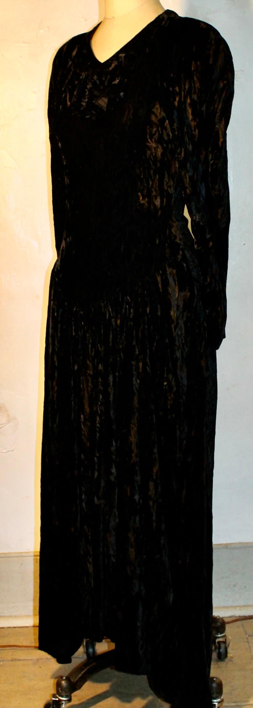 Of a 'crushed' black velvet. Approx. size 6. Dropped waist in front by design.  Padded shoulders. Bow in front below neckline. Length in front 50