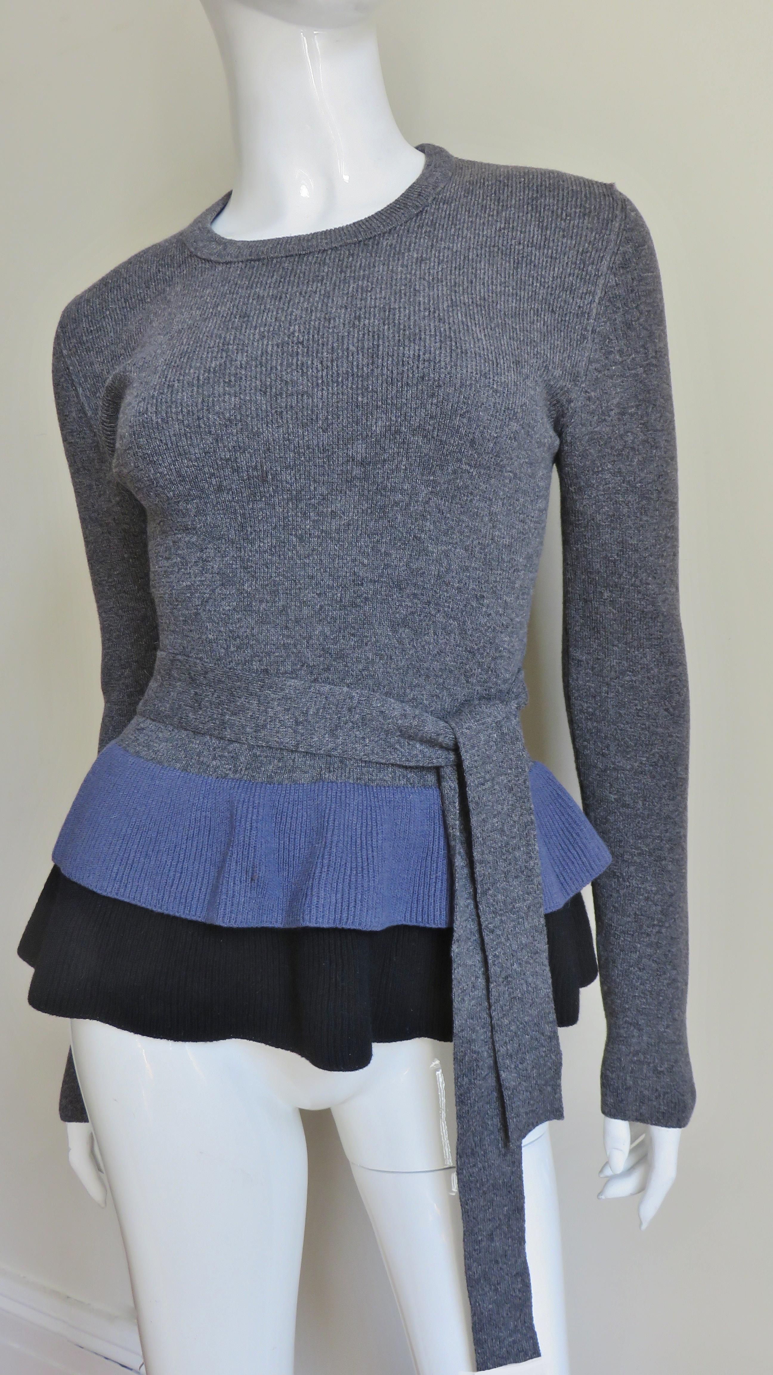 A gorgeous wool knit sweater from Sonia Rykiel in a black, purple and grey angora wool blend.   It has long sleeves, a crew neckline, a fabulous layered flounce or peplum bottom in black and purple and a grey tie at the waist.
Fits sizes Small,