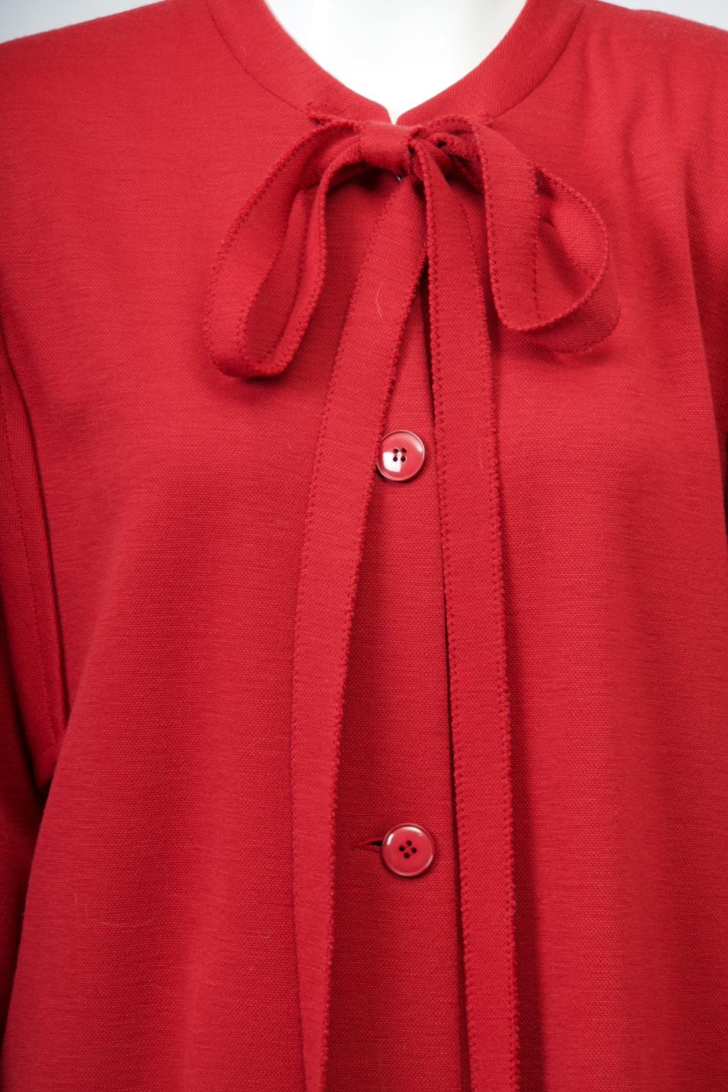 Manteau ou robe pull en laine rouge à double maille Sonia Rykiel des années 1980. Le nœud au cou, caractéristique de la créatrice, s'obtient en nouant les longues bandes de maille attachées sur le devant du col. Cette version est unique par la coupe