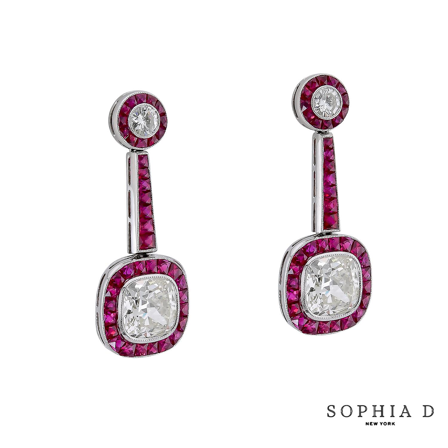 Platinum Art Deco drop earrings featuring two cushion-cut diamonds totaling 3.07 carats, framed by 2.00 carats of vivid French-cut rubies and topped with 0.26 carats diamond accents. A bold yet refined play of symmetry and color.

Sophia D has been