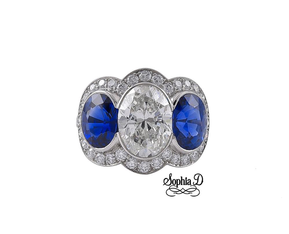 This 3-stoned ring set in platinum by Sophia D. features a 3.03 carat oval diamond center, 4.27 carats in total of two blue sapphires accentuated with .71 carat of small diamonds. Available for resizing.

Sophia D by Joseph Dardashti LTD has been