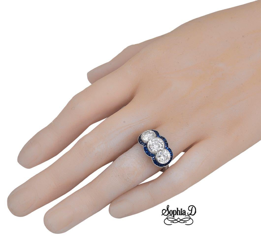 Dreisteiniger Platinring mit einem runden Diamanten mit einem Gewicht von 2,25 Karat in der Mitte, umgeben von runden Diamanten mit einem Gewicht von 0,06 Karat und einem blauen Saphir mit einem Gewicht von 1,00 Karat. 

Verfügbar für
