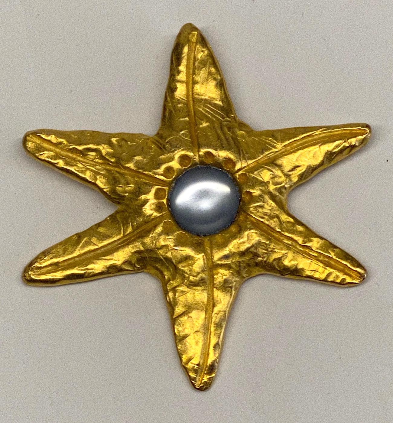1980s satin gold martele' finish abstract star brooch by French desinger Sophie Goetsch. The center is set with a frosted light blue lucite cabochon. Brooch measures 3.25 inches in diameter and .38 of an inch high not including the pin. The back has