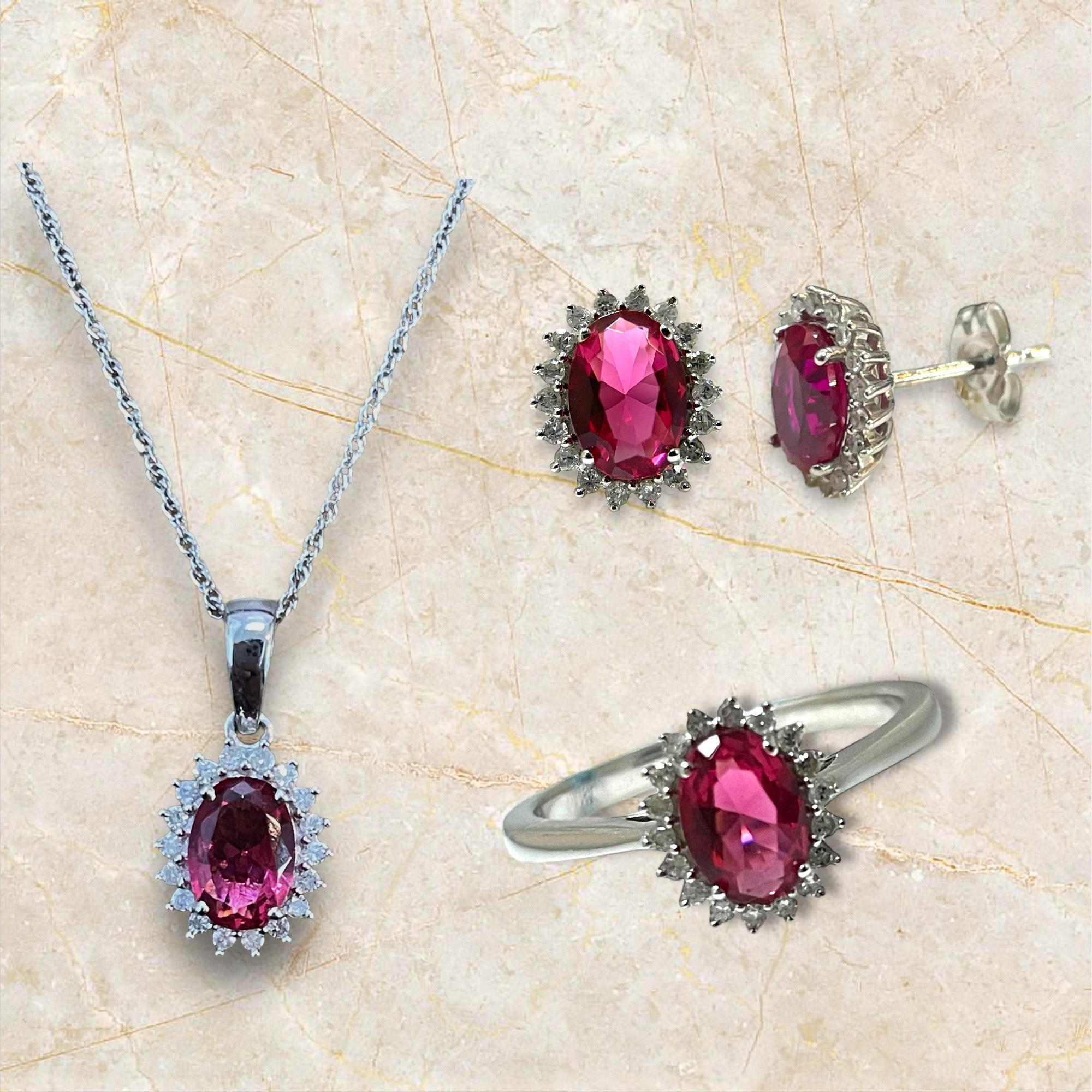This stunning 14K white gold jewelry set features a captivating oval red gemstone at the center of each piece, surrounded by a halo of sparkling accents. The set includes a pendant necklace, a pair of earrings, and a matching ring, all designed to