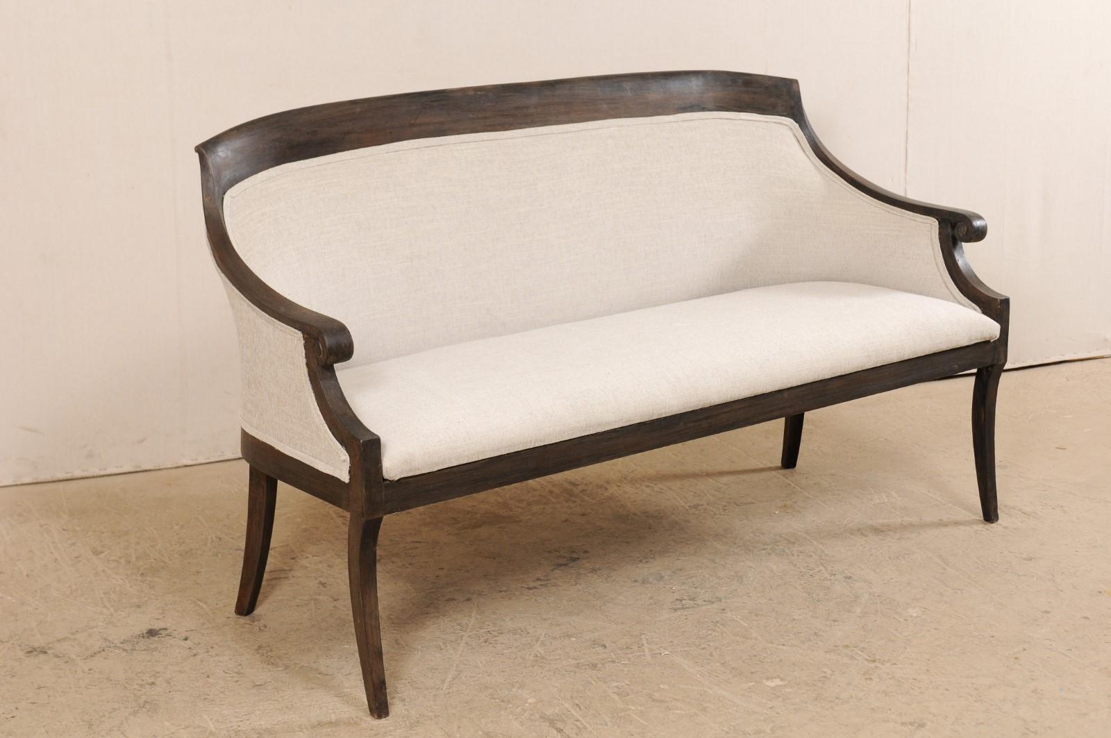 A Swedish upholstered settee from the mid-19th century. This antique sofa from Sweden, just over 5 feet in length, features a beautifully wrapped back with a raised, flat-edged wooden crest rail which flows gently down the arms into curled knuckles.
