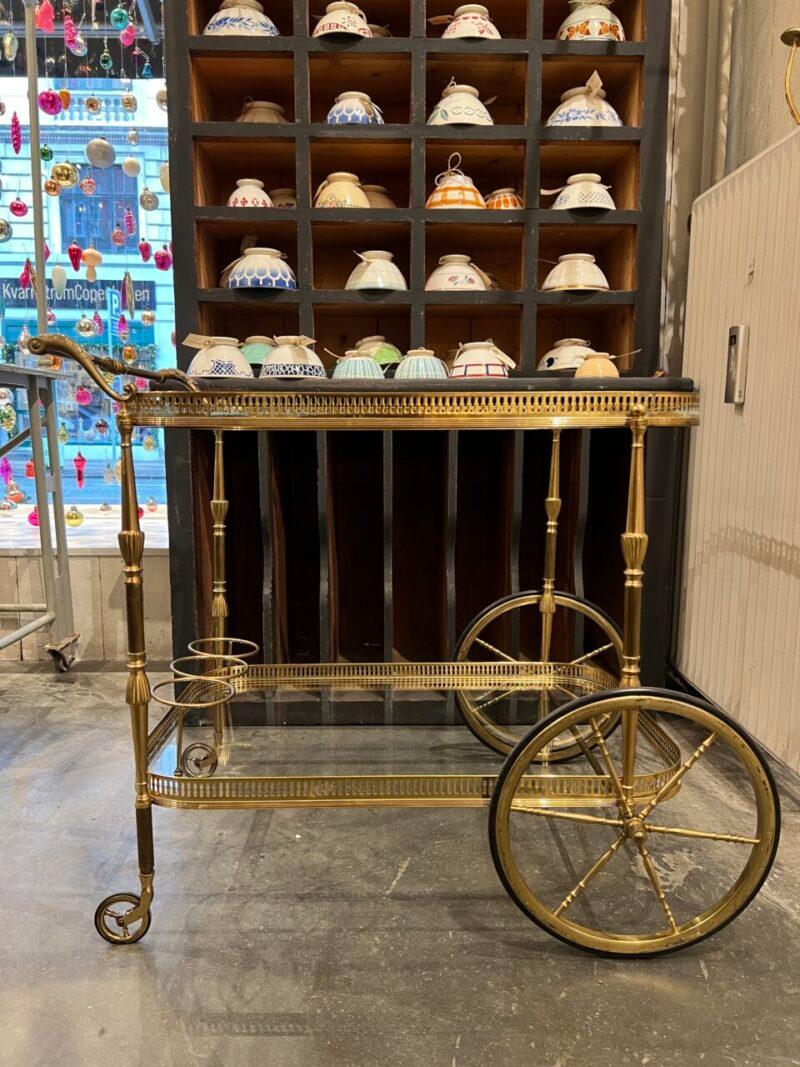 Elegante carrito de bar/carro de servir francés de mediados de siglo, con armazón de latón de calidad sobre 2 ruedas grandes y 2 pequeñas.

También está equipada con 2 tapas de cristal transparente, un portabotellas y unas asas extremadamente