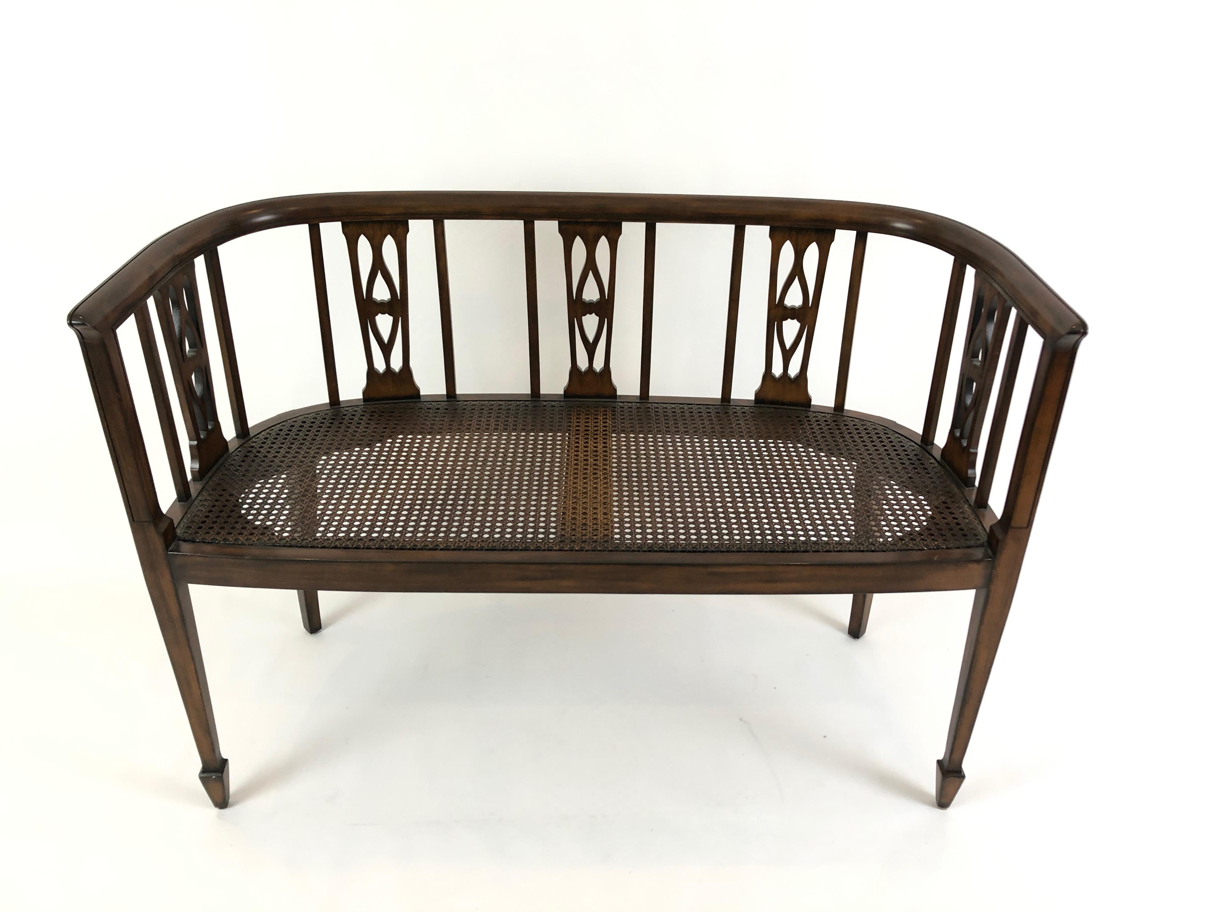 Refined fruitwood settee having lovely curved back with open fretwork, tapered legs and excellent condition caned seat. Custom cushion in a traditional small pattern and neutral color palette is included. Seat height without cushion 17.25.