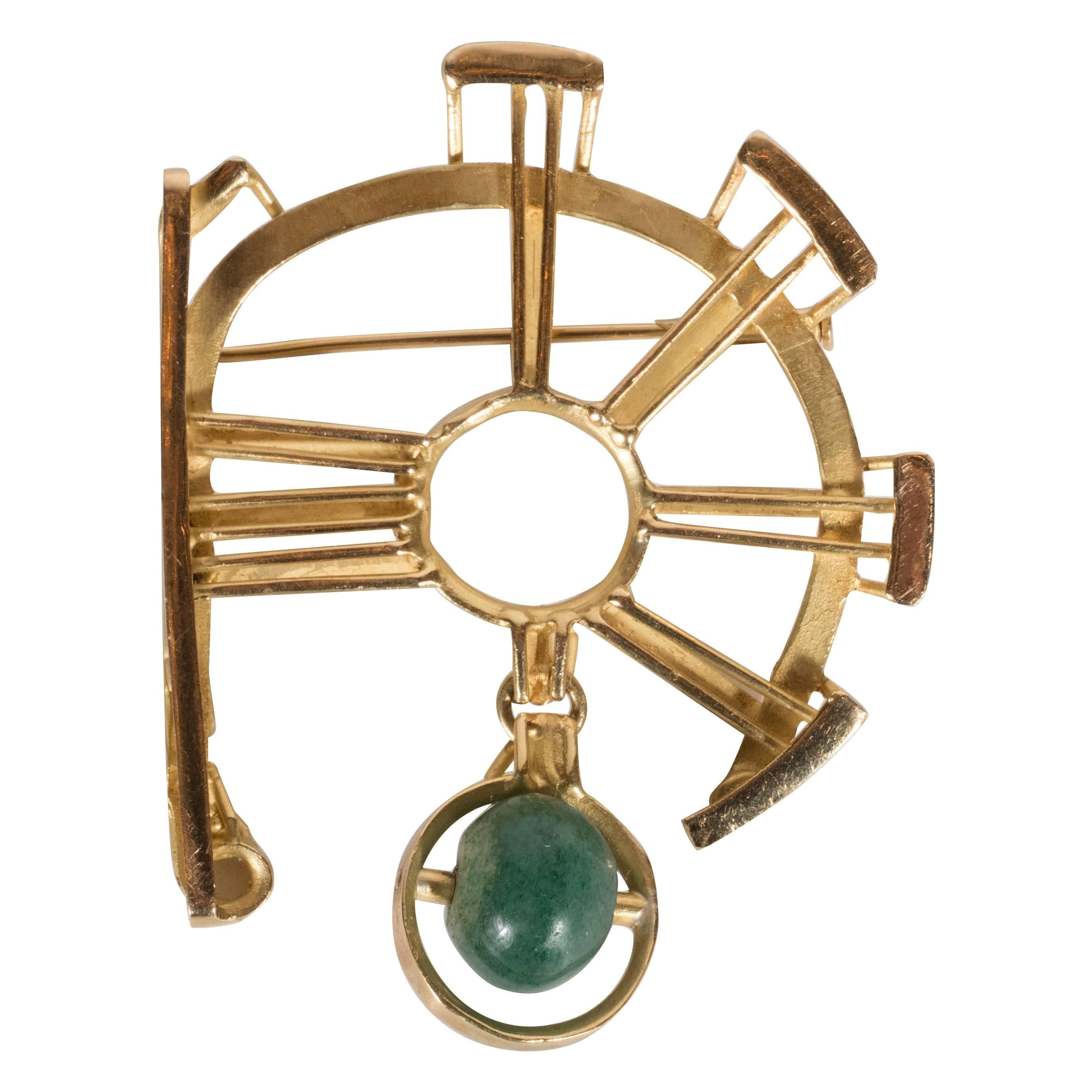 This dynamic geometric brooch features vertical stokes in 18 karat yellow gold emanating from a central circular form. A serpentine jade wheel on a horizontal axis hangs from one of these stokes, encompassed by a circle that echoes the central form.