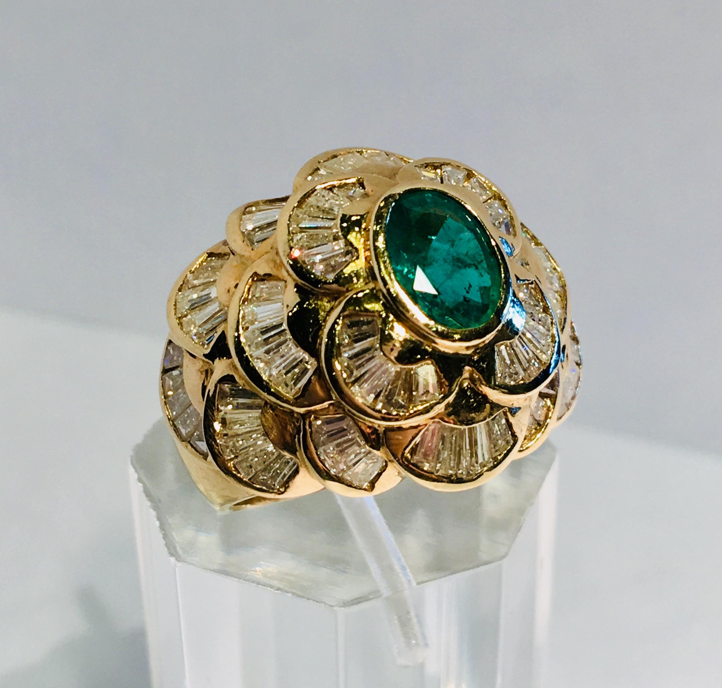 Elegant, stately, dome-shaped, 14 karat yellow gold high fashion cocktail ring with a very wide band features an oval cut emerald with vivid green color, bezel-set and surrounded by 18 three-dimensional layers of invisibly-set diamond baguette