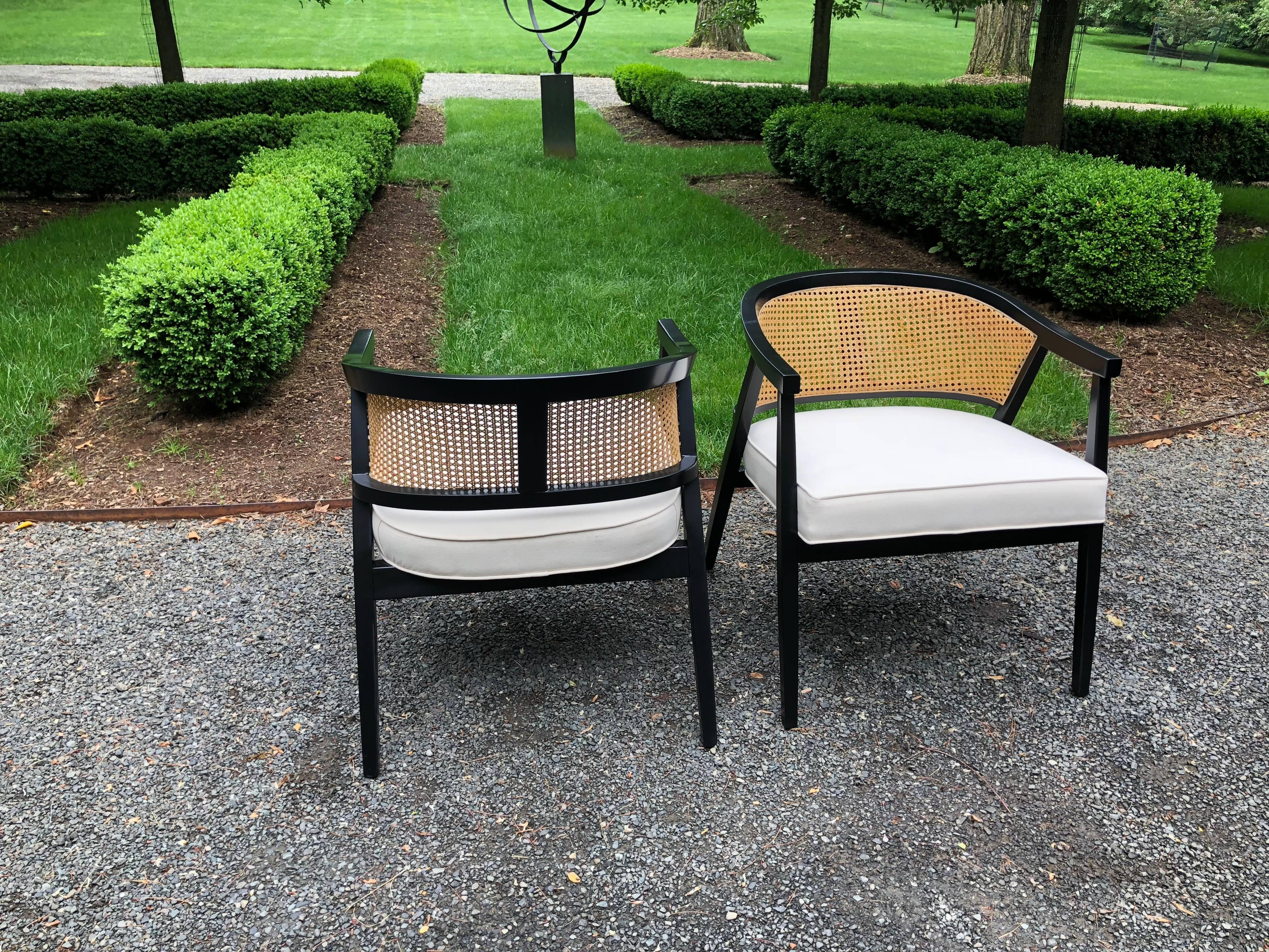 Sophisticated pair of ebonized caned barrel back chairs having black painted frames, caned backs and white cotton freshly upholstered seats. Measures: Seat height is 18; seat depth 21.5 and seat width 22. One repaired small break in caned back which