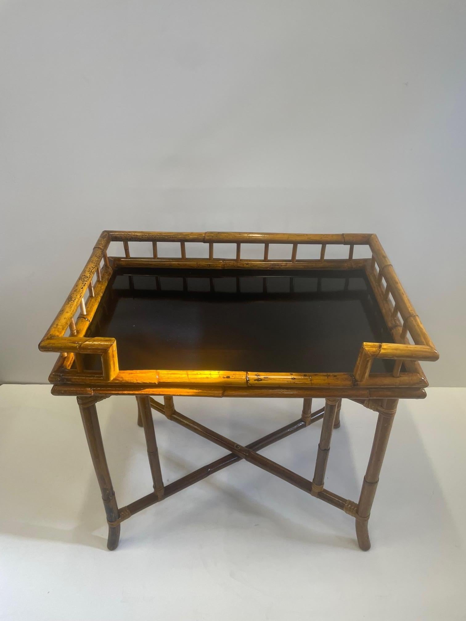 Sophisticated bamboo rattan tray on stand that makes a cool bar or side table having rattan gallery and stylish splayed legs with stretcher. The honey color of the rattan is offset by the black laminate surface of the tray. Tray top is 23.5 H.