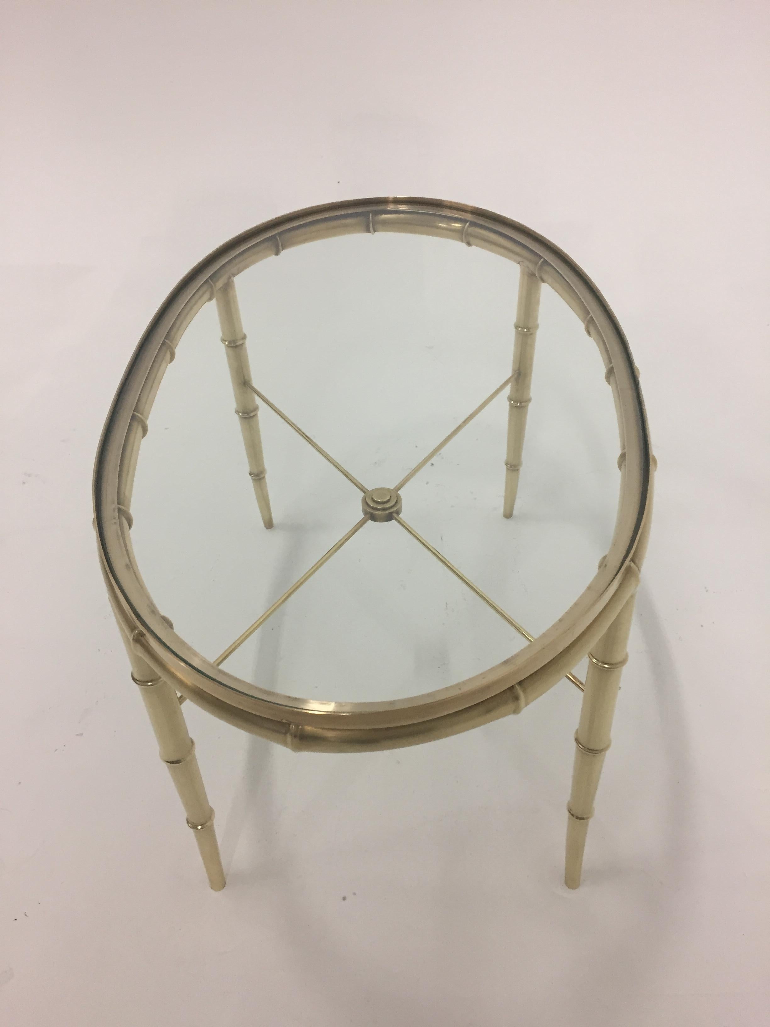 Very elegant solid brass vintage oval coffee table having faux bamboo style, gorgeous thin stretcher beneath with pretty center finial, glass top and newly polished lustre.