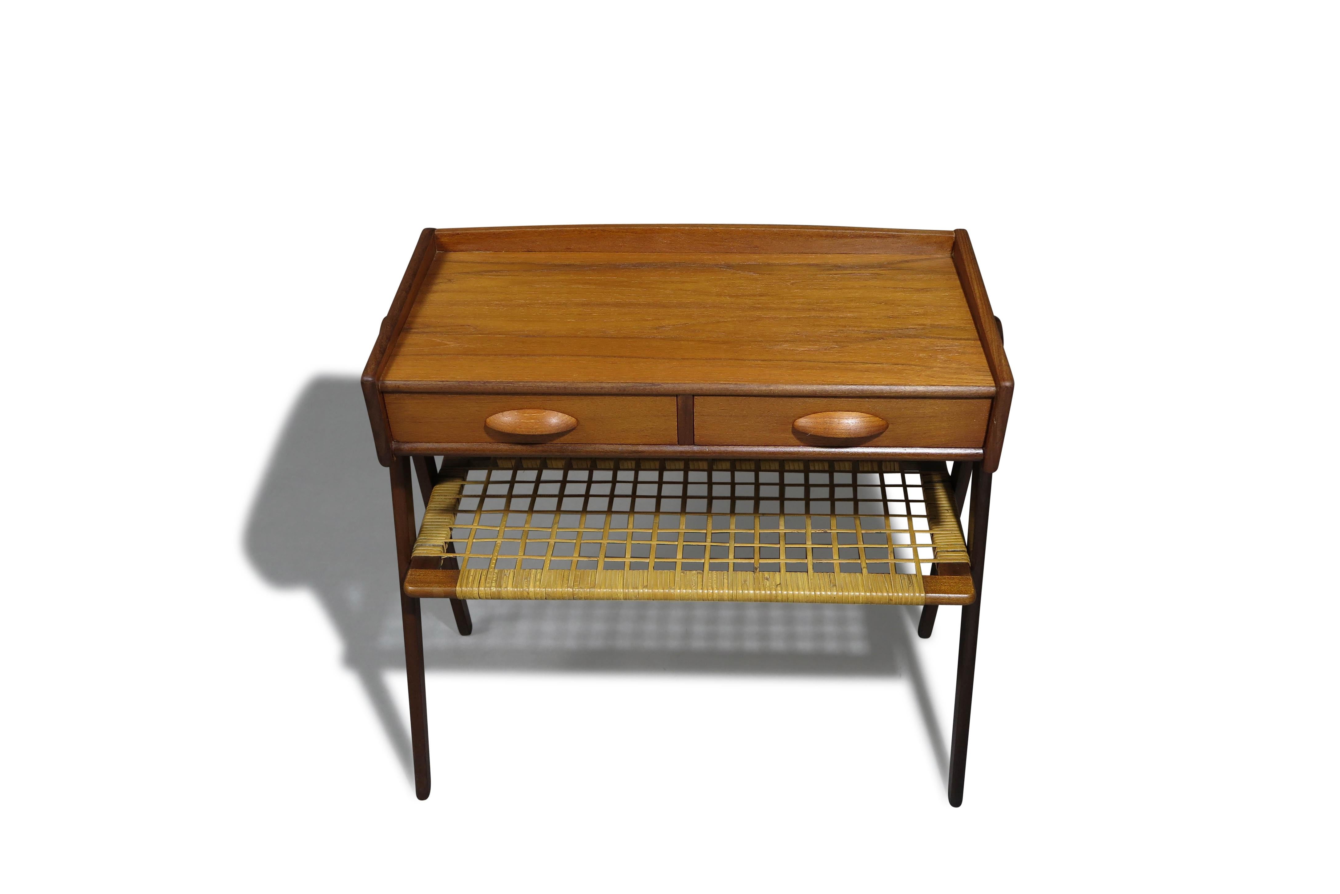 Mid-century Danish teak side table designed by Søren Rasmussen, Denmark, circa 1960s. Crafted from teak, it features two drawers with carved pulls and a woven rattan shelf. The cabinet is raised on V-shaped solid teak legs. Fully restored, it is in