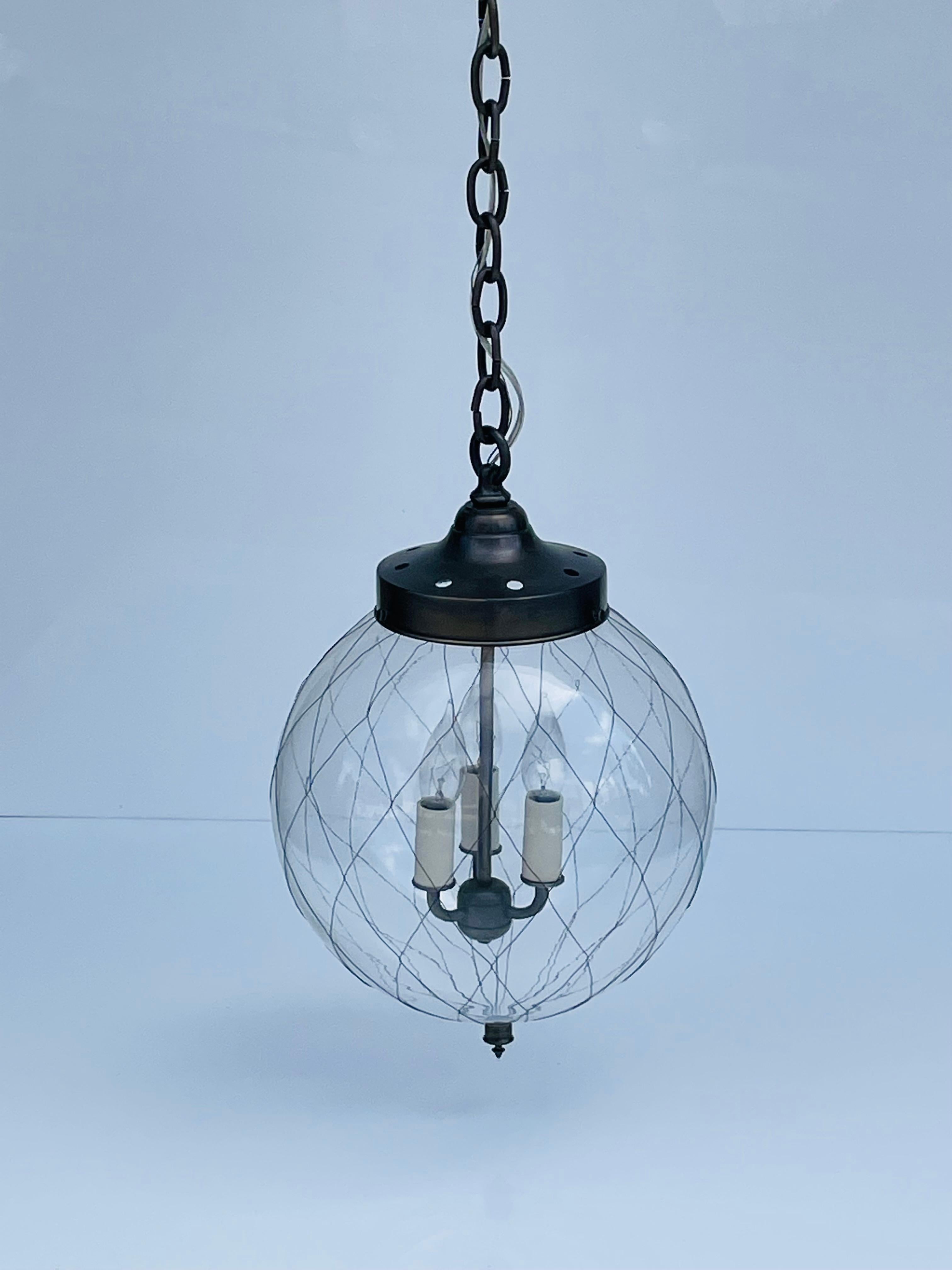 This versatile lantern references a form of historical factory lighting where the glass was netted for safety. The thick clear mouth-blown glass is wrapped in a hand-woven wire fabric. Each with slight, unique variations due to the hand-made nature