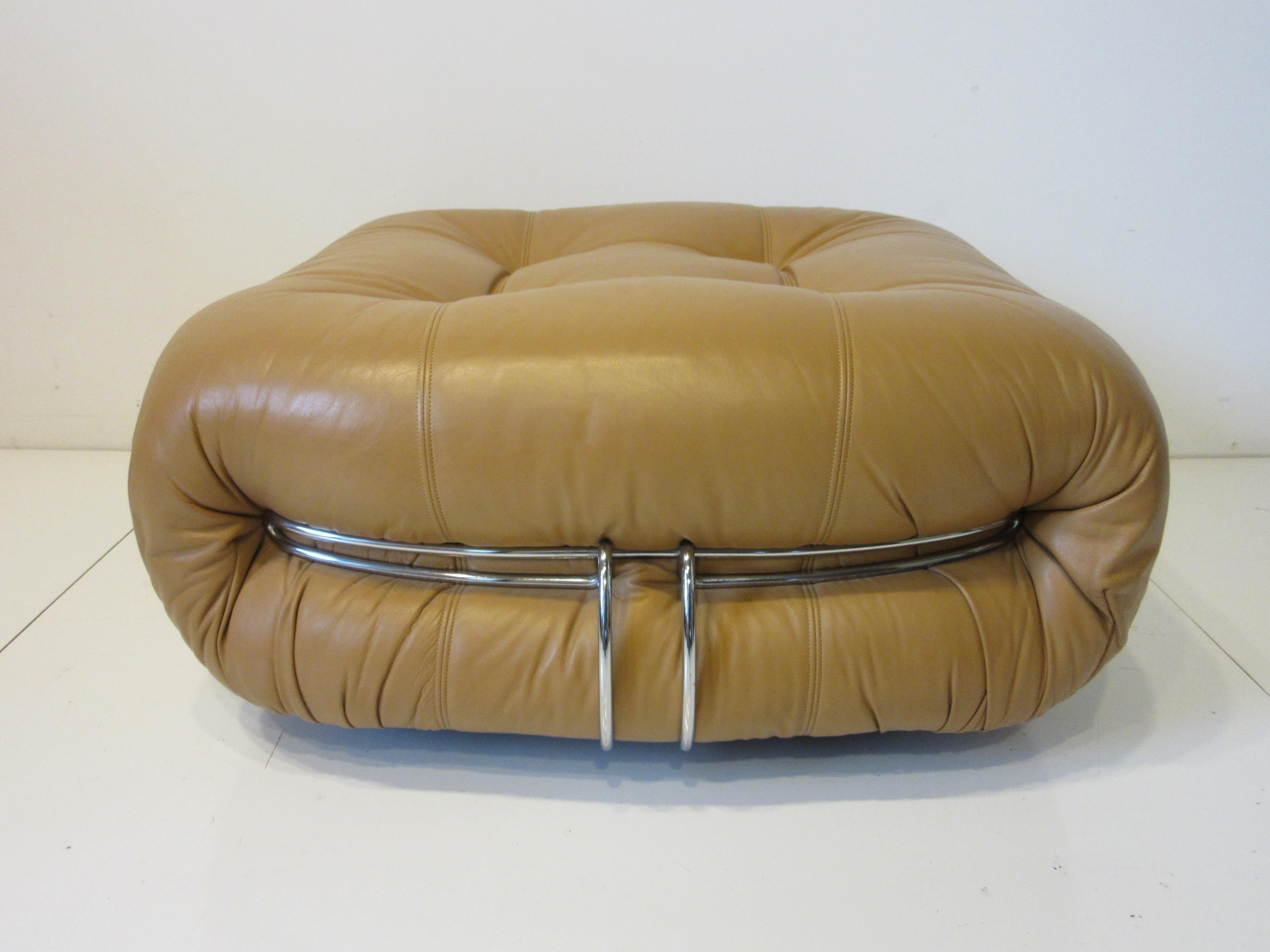 A saddle colored leather ottoman on rollers with tufted and stretched form having chromed metal banding to each end. An iconic piece of 1970's Italian design by Afra and Tobia Scarpa model # A202 retaining the manufactures labels to the bottom by