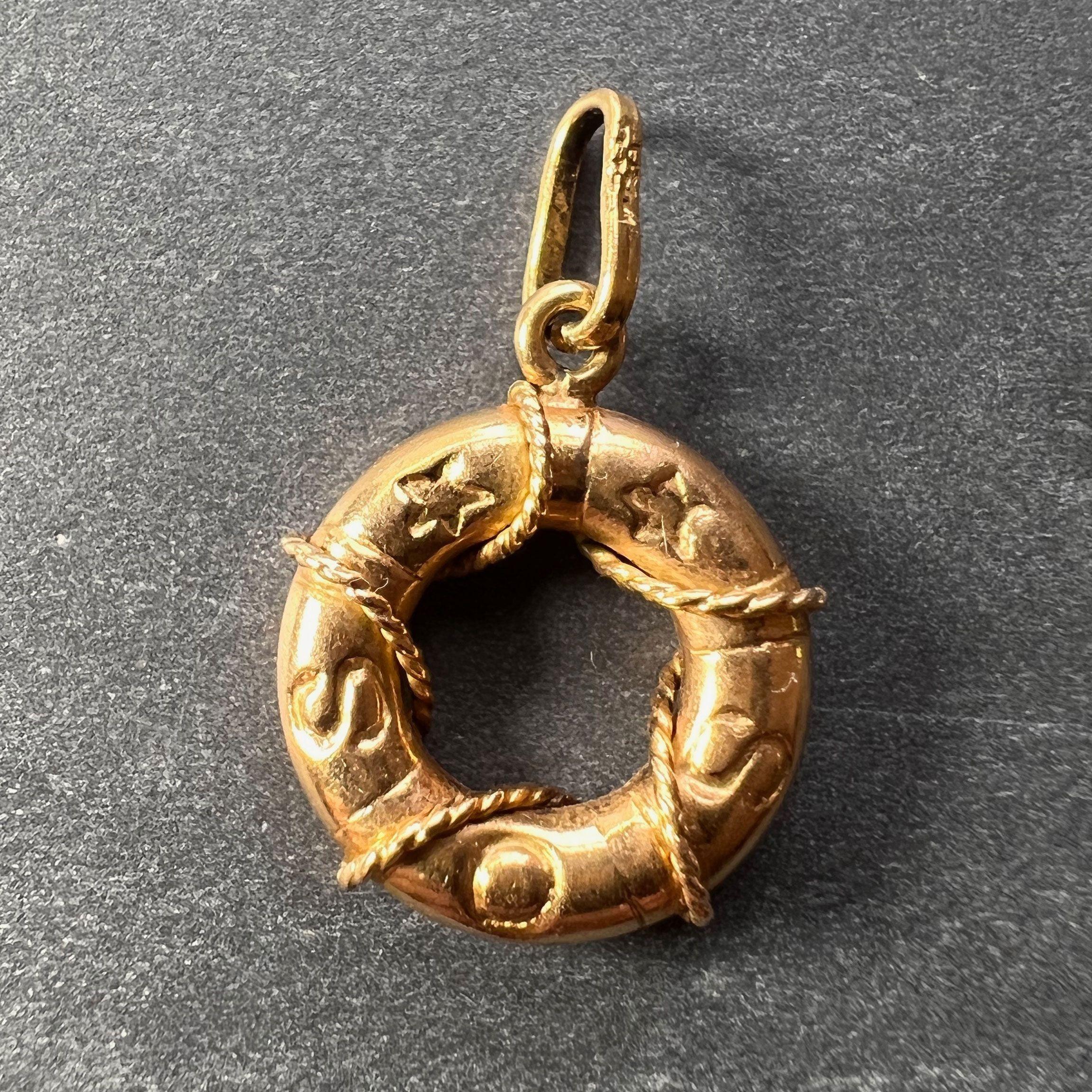 An 18 karat (18K) yellow gold charm pendant designed as a life preserver or buoy wrapped with rope and marked SOS. Stamped 750 for 18 karat gold to the jump ring.

Dimensions: 1.7 x 1.4 x 0.4 cm (not including jump ring)
Weight: 1.50 grams