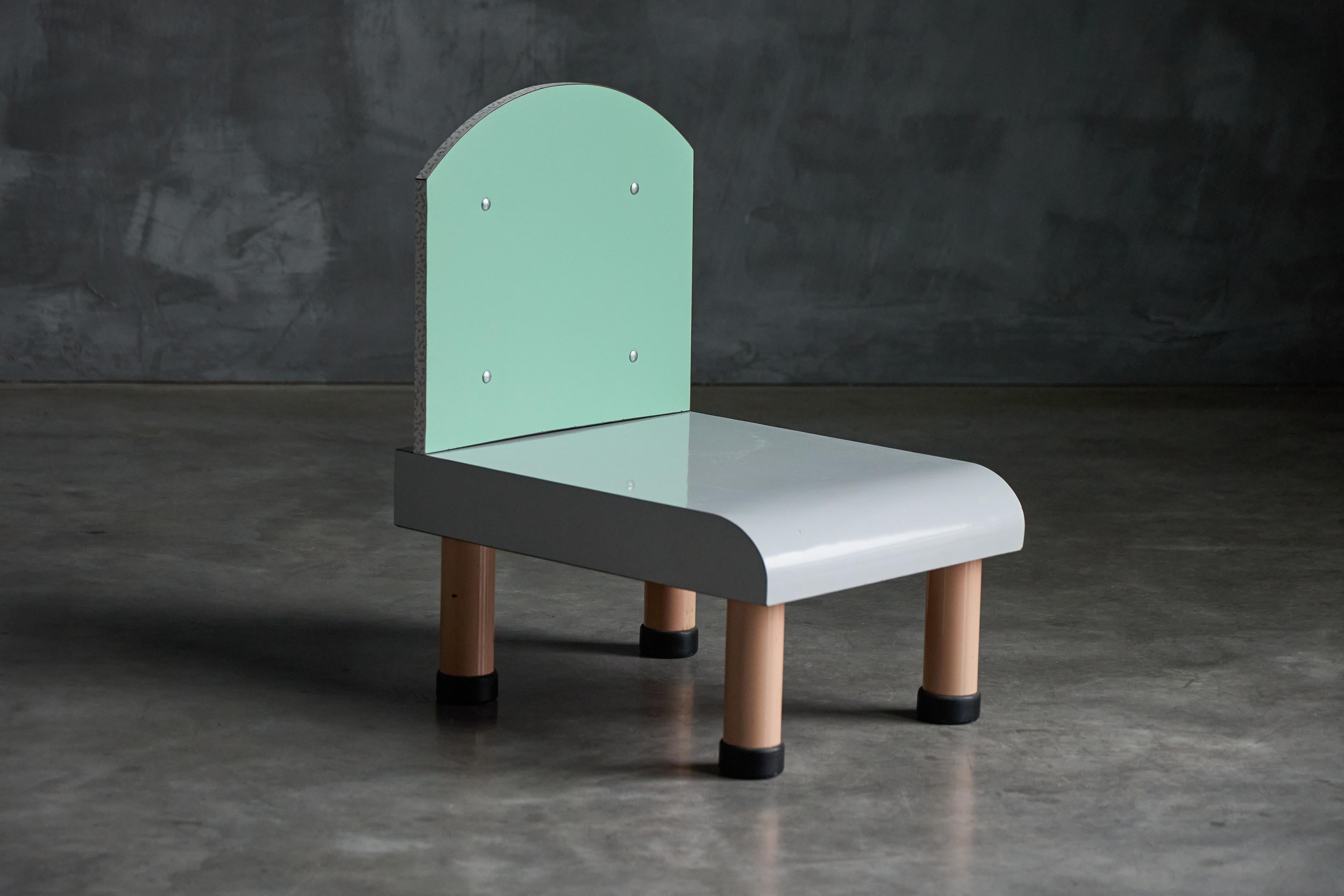 Playful and sophisticated, this Memphis-style chair captures the essence of postmodern design with its bold shapes and pastel shades. The backrest features a curved silhouette in a refreshing mint green, enhanced with subtle silver rivet detailing