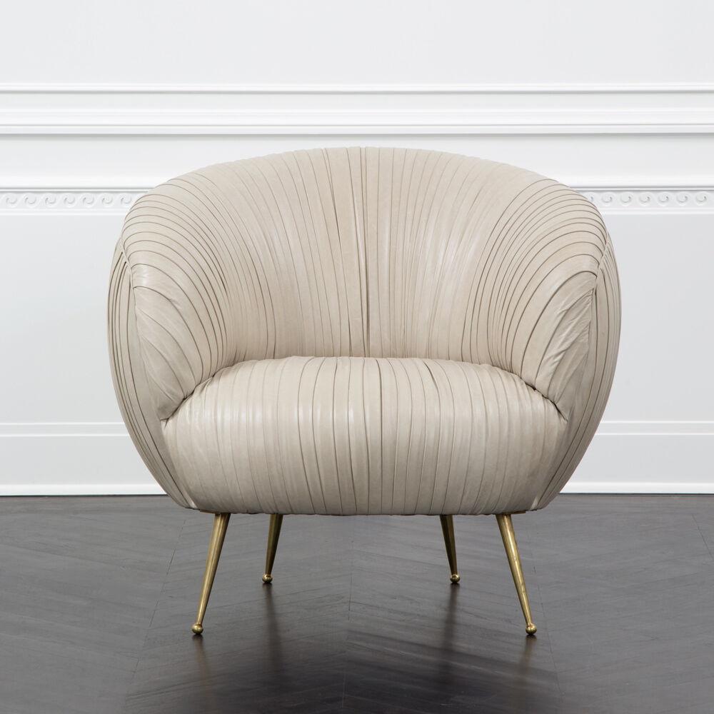 With its curvilinear form, bold massing, and thoughtful detailing, the Souffle chair is a modern icon. This chair features solid cast burnished brass legs and an artisanal ruched body which is available in a curated selection of leathers. Non-ruched