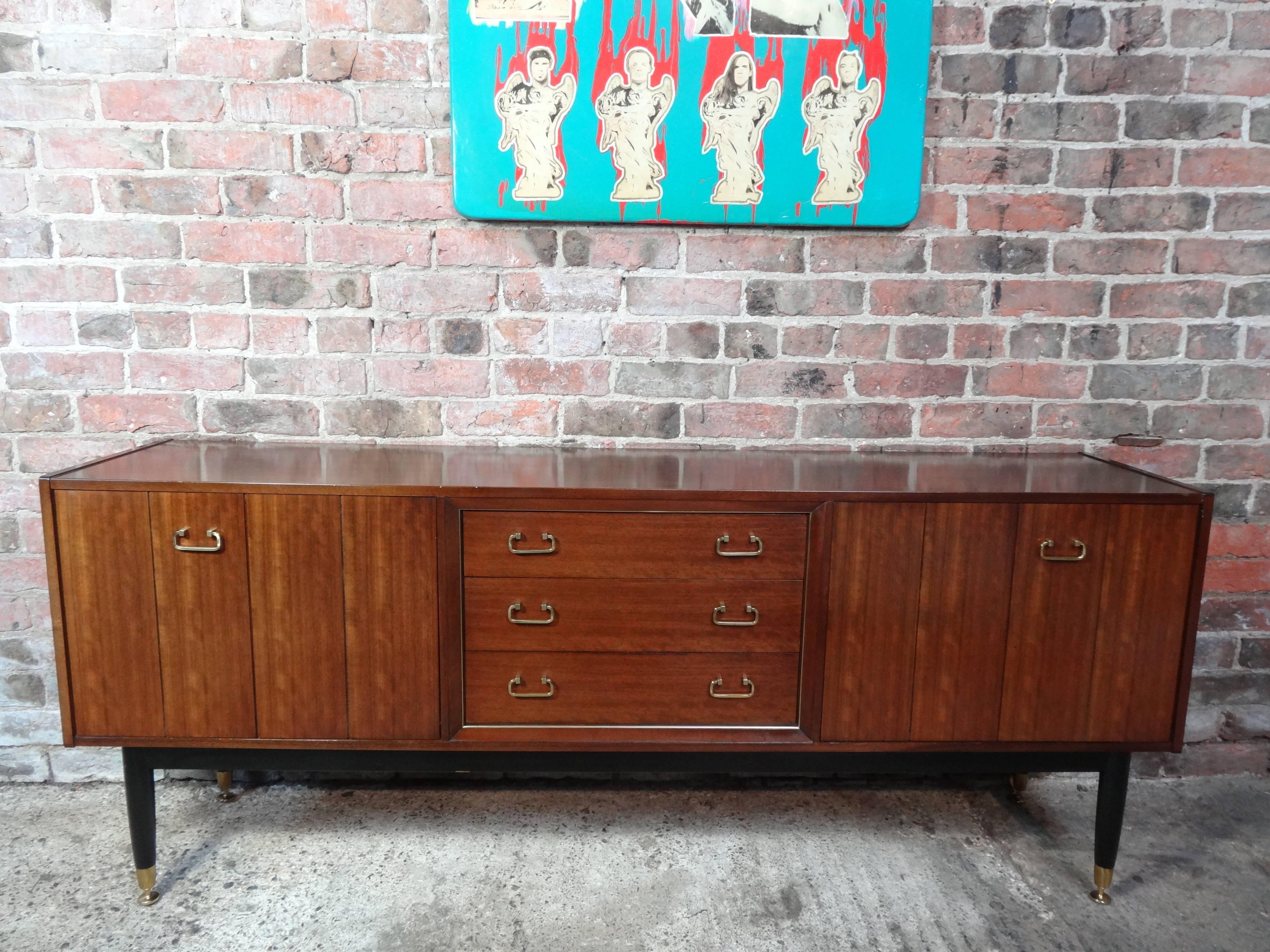 Sought after vintage retro E Gomme teak sideboard with brass handles and feet its from early 1950s. It has three drawers, cupboard space with lovely brass handles on the byfolding doors. Credenza is in very good original condition.