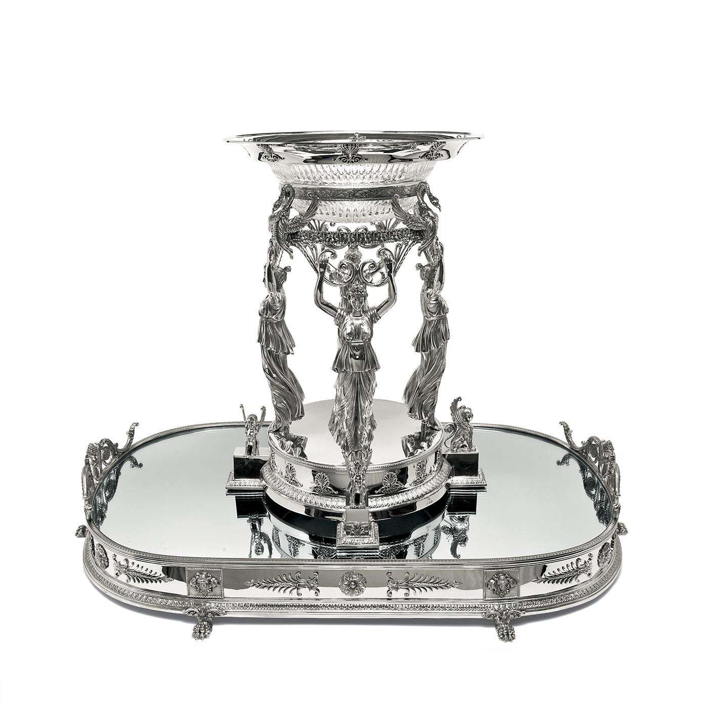 This superb centerpiece is entirely crafted in silver using artisanal methods and is inspired by the lavish, neoclassical Empire style developed with Napoleon at the beginning of the 19th century. It is made up of three elements: the oval base with