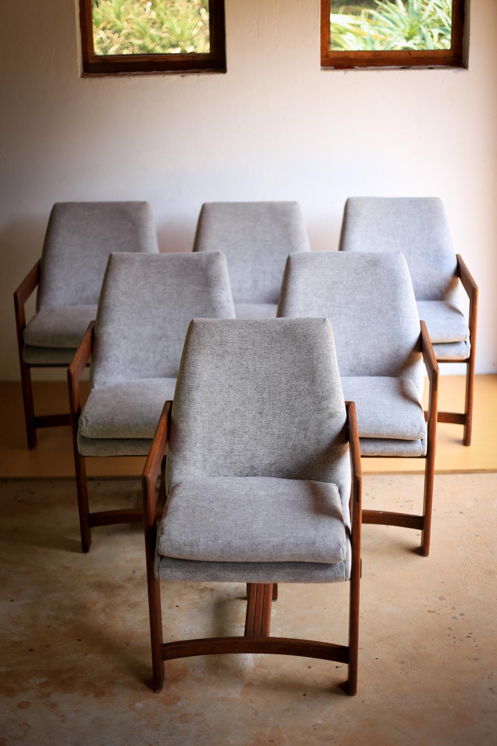 A set of six cubist African teak (kiaat wood) dining chairs designed and made in the 1960s in South Africa. The unique, strong three-legged frame supports a tub type seat with an angled back rest and loose seat cushion, upholstered in a light grey,