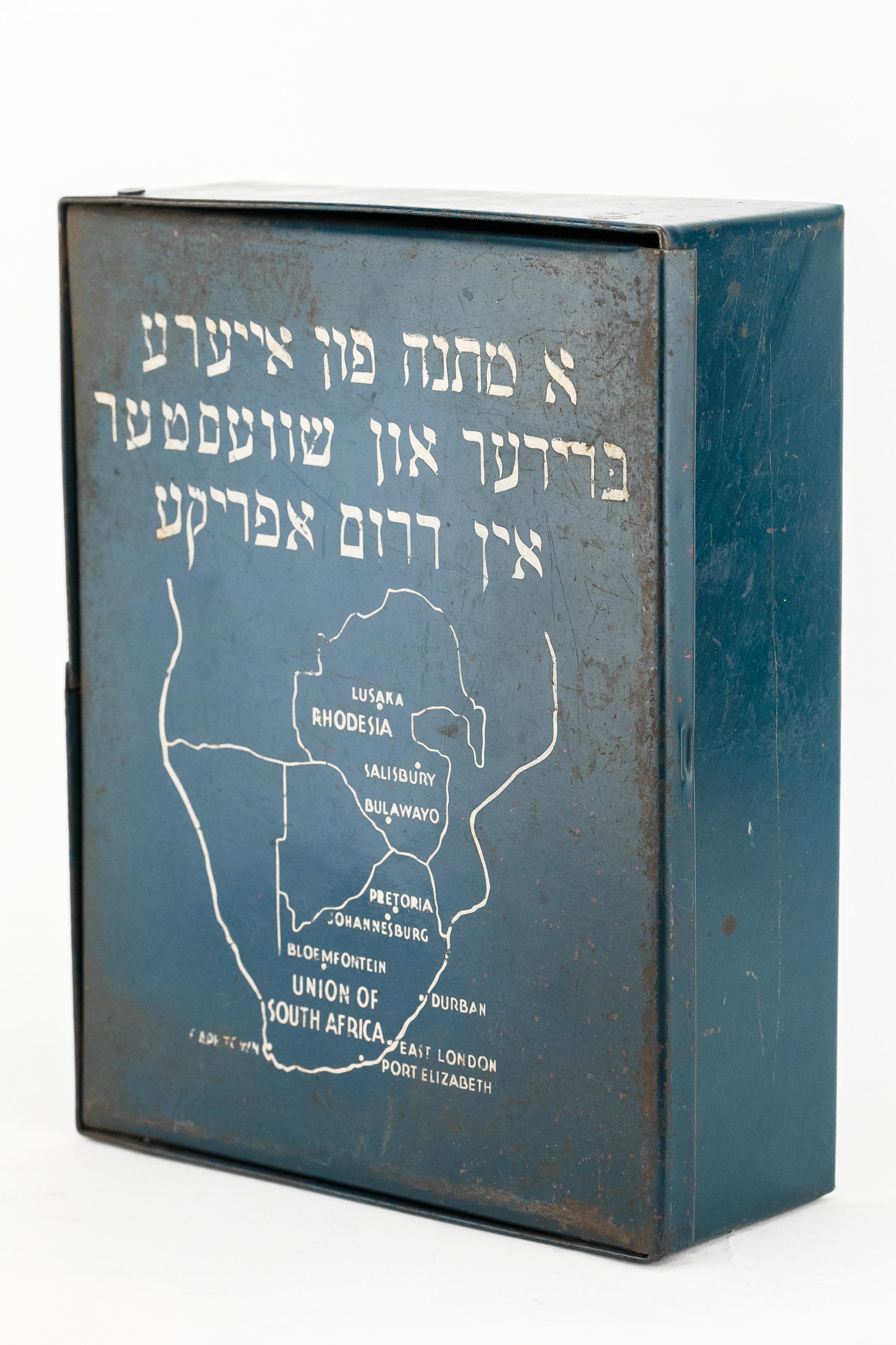 Caja metálica de material escolar enviada por el Llamamiento Judío de Guerra de Sudáfrica al campo de desplazados de Wels (Austria), 1947.
Pintado en azul y blanco con el mapa de Sudáfrica, e inscripción en hebreo: 