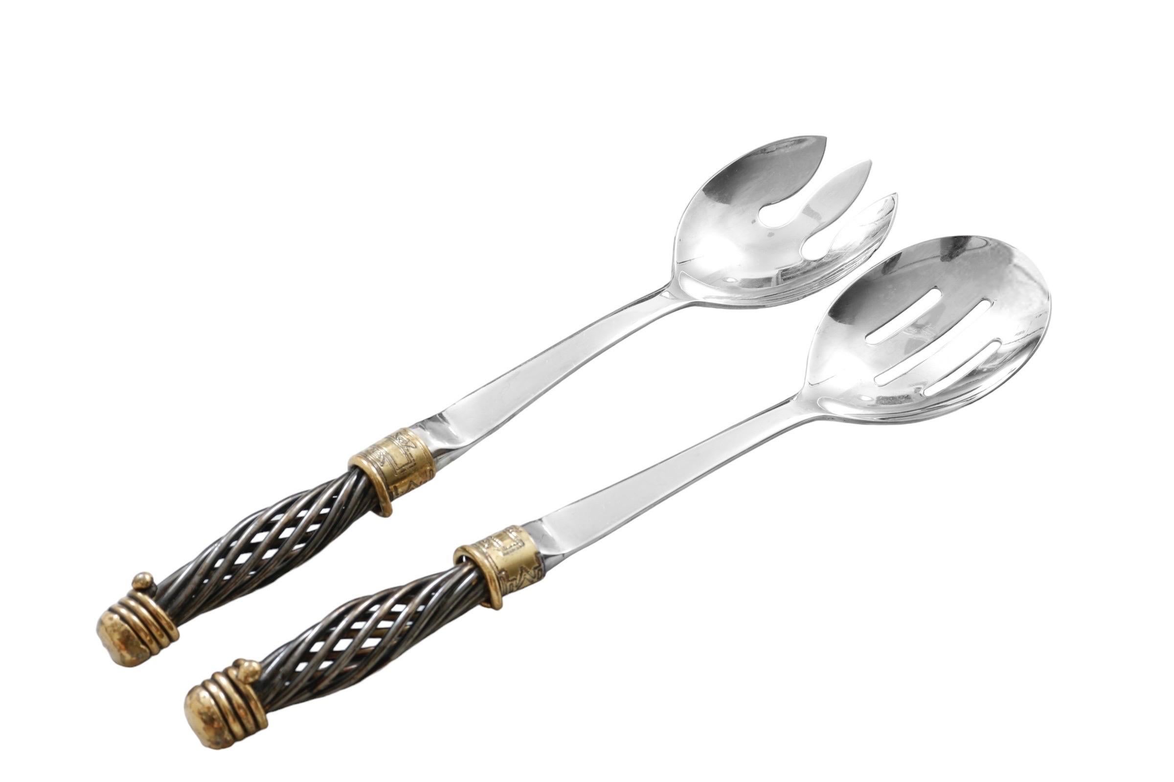 Un service à salade en acier inoxydable composé d'une cuillère et d'une fourchette fabriqué par Copper Craft. Les extrémités de service en acier inoxydable sont reliées à des poignées en métal forgé dans un design en spirale, avec du laiton martelé,