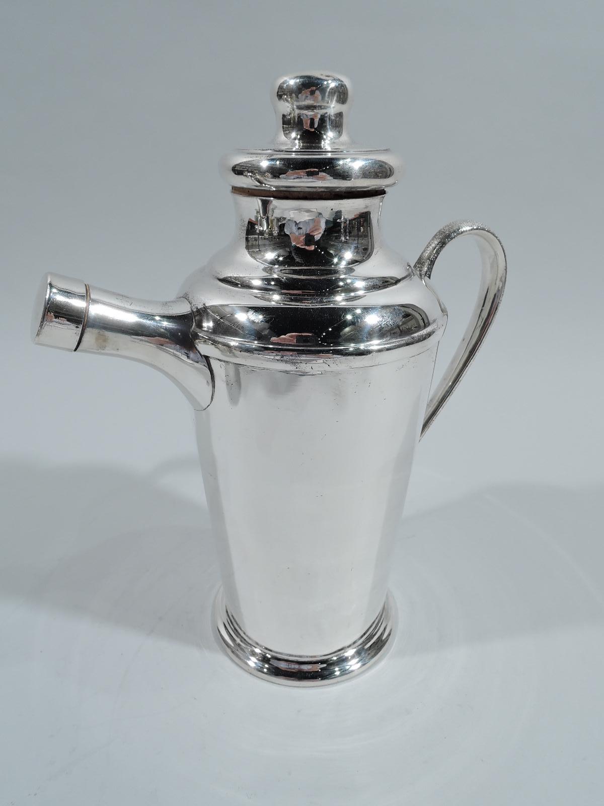 Mid-Century Modern sterling silver cocktail shaker. Straight and tapering body and skirted foot. Stepped shoulder and snug-fitting cover with cork plug. Stippled high-looping handle and assertive stubby spout with cork-plugged cap. Functional with