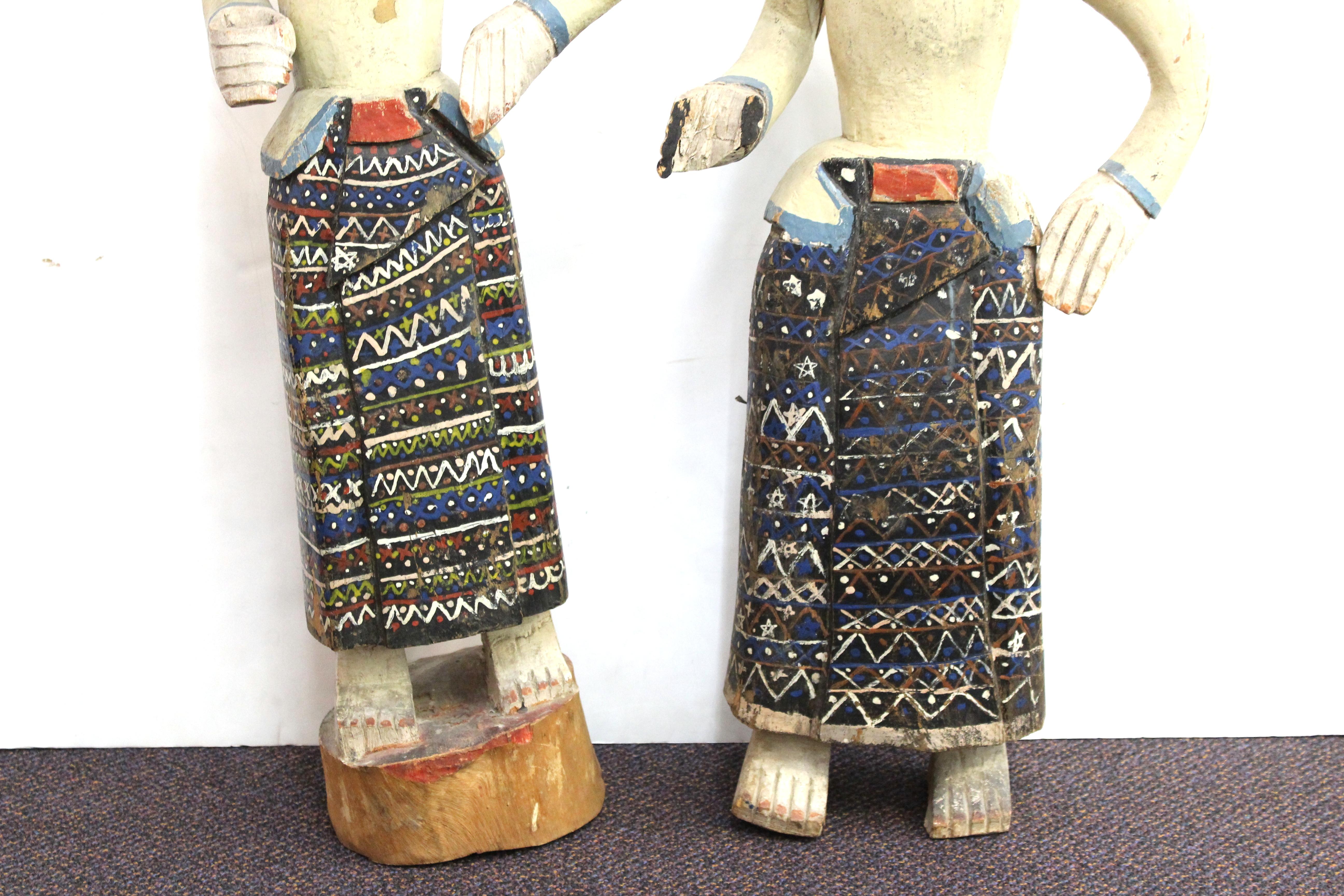 South-East Asian pair of carved and hand-painted wood figures of standing men with articulated arms, in colorful sarongs and traditional tribal headgear, one standing on a block, the other one standing flat. Both have some paint wear, the shorter