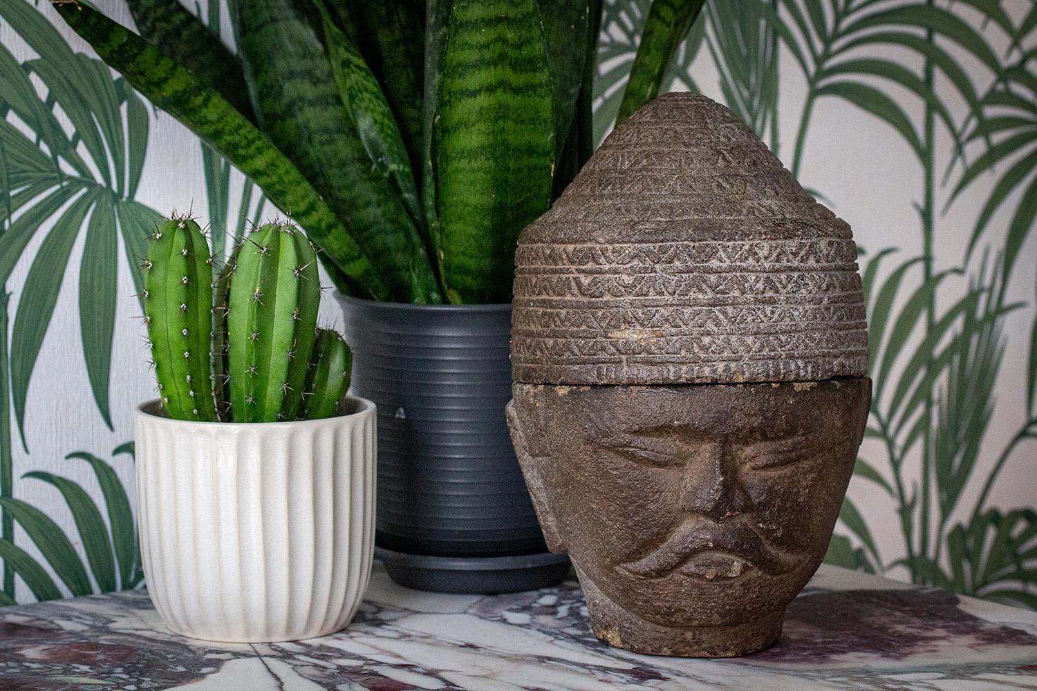 Unusual carved stone head with storage compartment. The South East Asian grey stone carved in the shape of a male head wearing a conical hat and having a moustache. The hat lifts to reveal a storage cavity within with obvious signs of hand-made