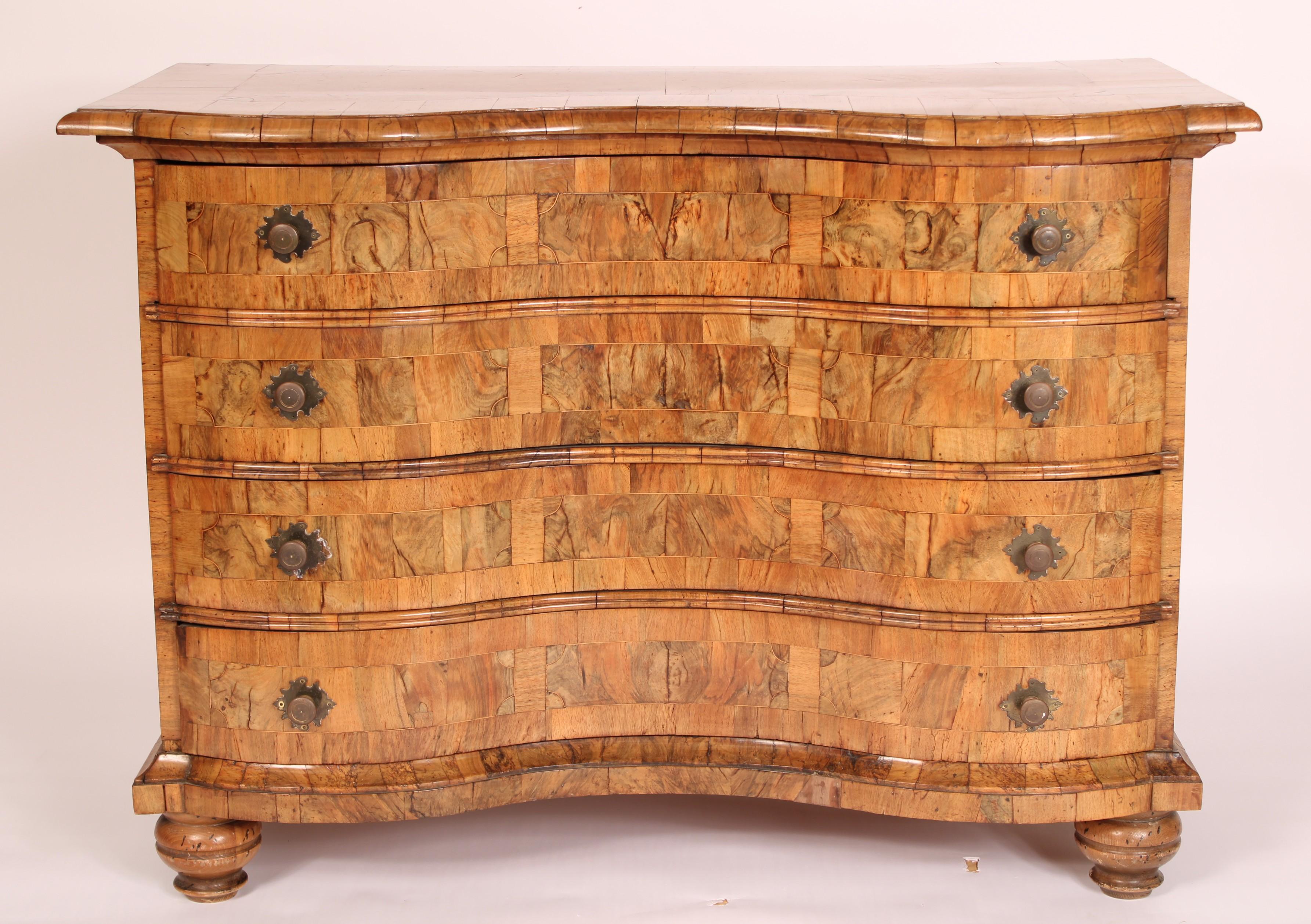 Serpentinenförmige Kommode aus süddeutschem Nussbaum und Wurzelholz, um 1835. Die Oberseite ist mit einer eingelegten Wurzelholzplatte versehen, die von einer Querleiste aus Nussbaumholz eingefasst ist. Darunter befinden sich 4 Schubladen mit einer